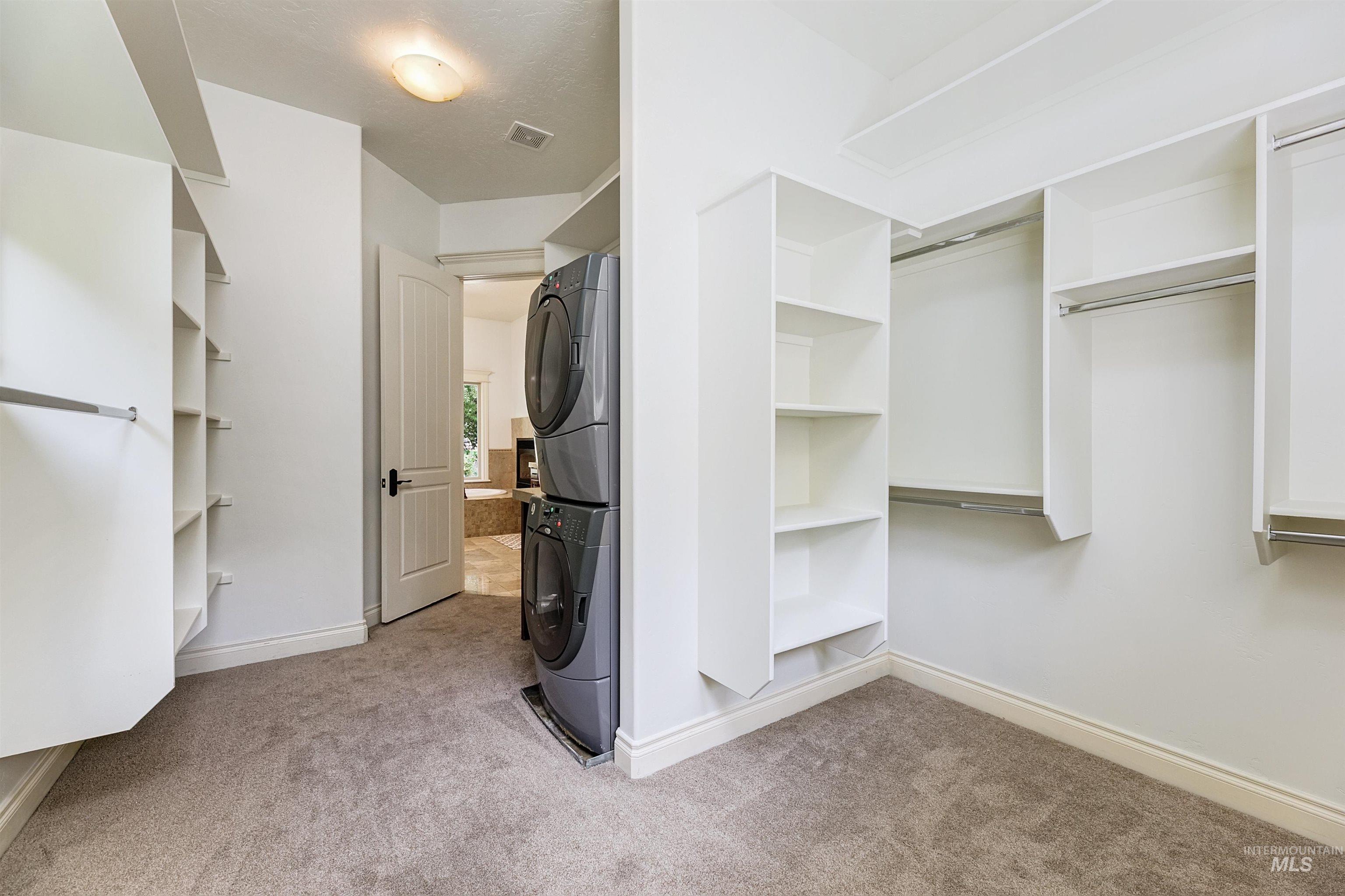 Walk in closet with light colored carpet and estacked washer and dryer
