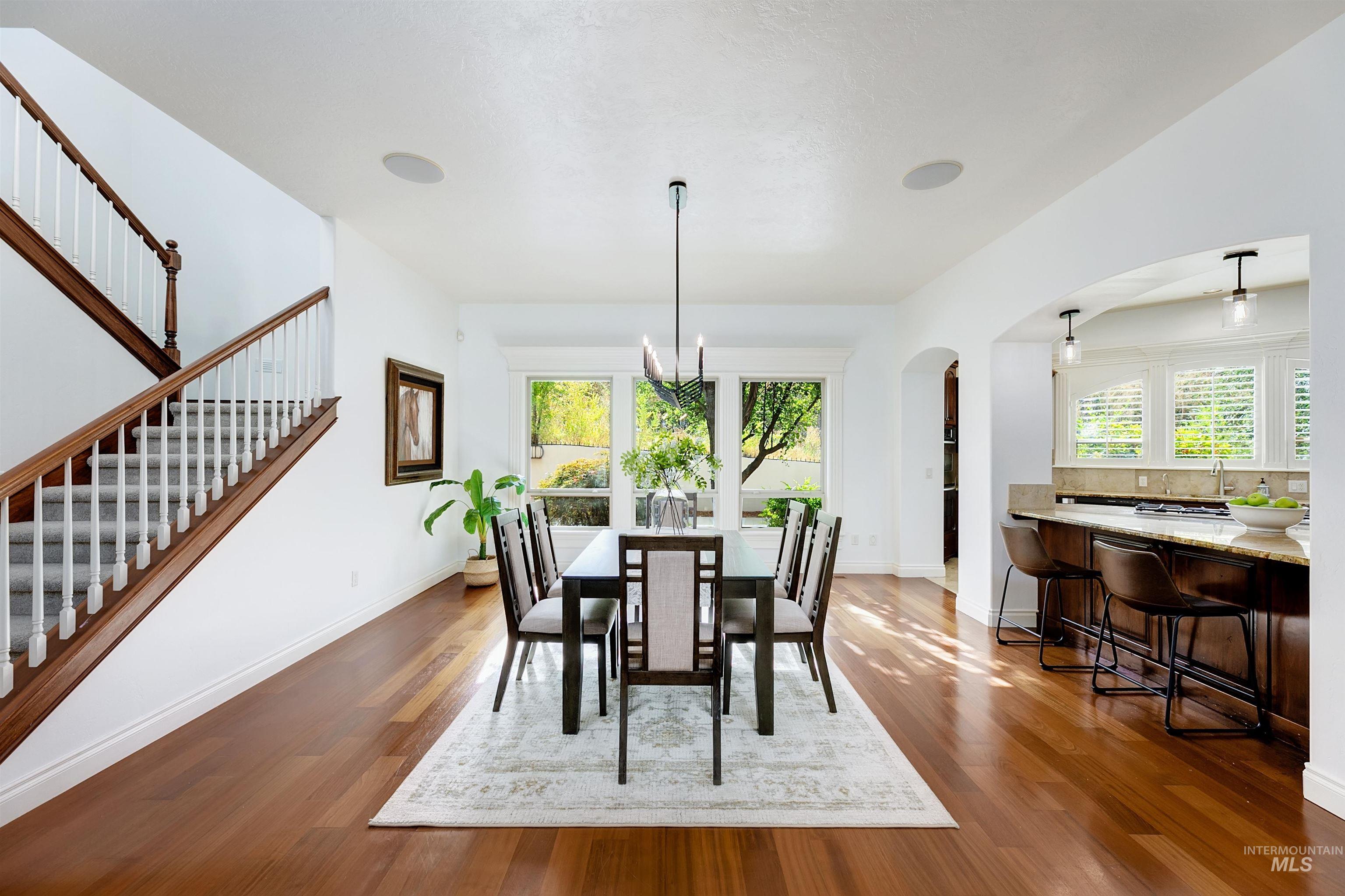 Dining space featuring dark wood-style floors, a chandelier, arched walkways, and stairs