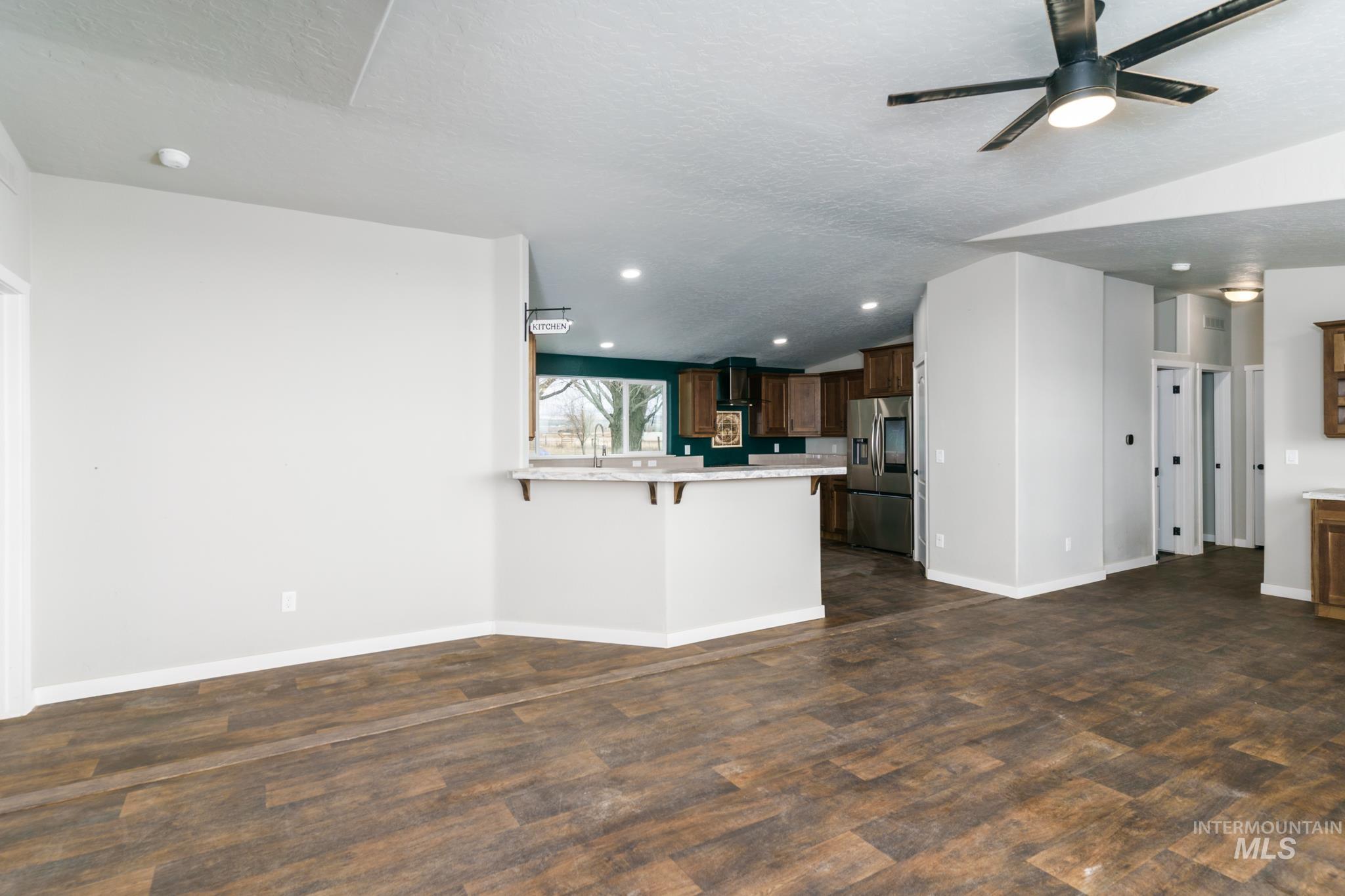Unfurnished living room with vaulted ceiling, a ceiling fan, a textured ceiling, dark wood-style flooring, and recessed lighting