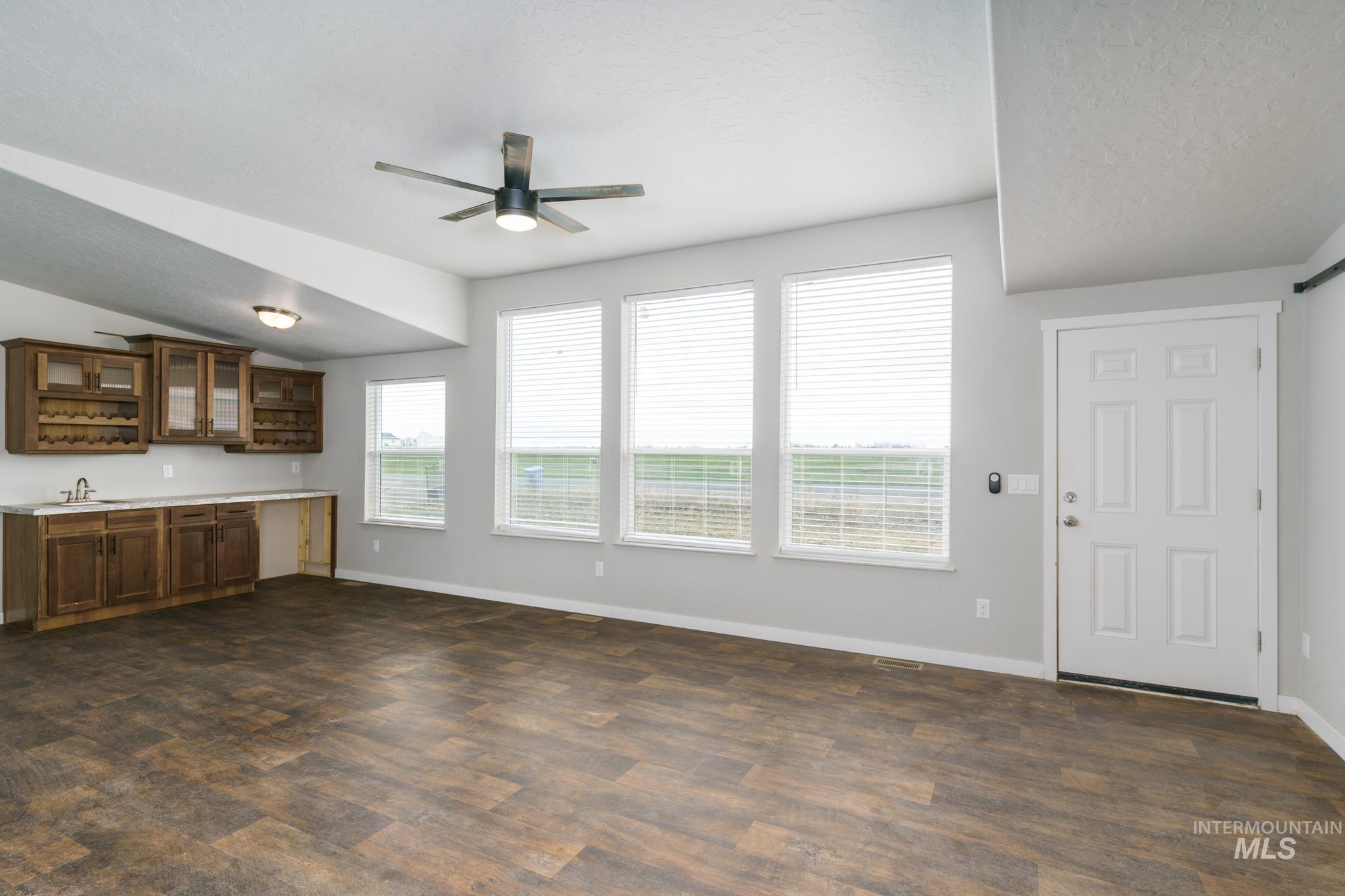 Unfurnished living room featuring dark wood-style flooring, a ceiling fan, bar with sink, and a textured ceiling