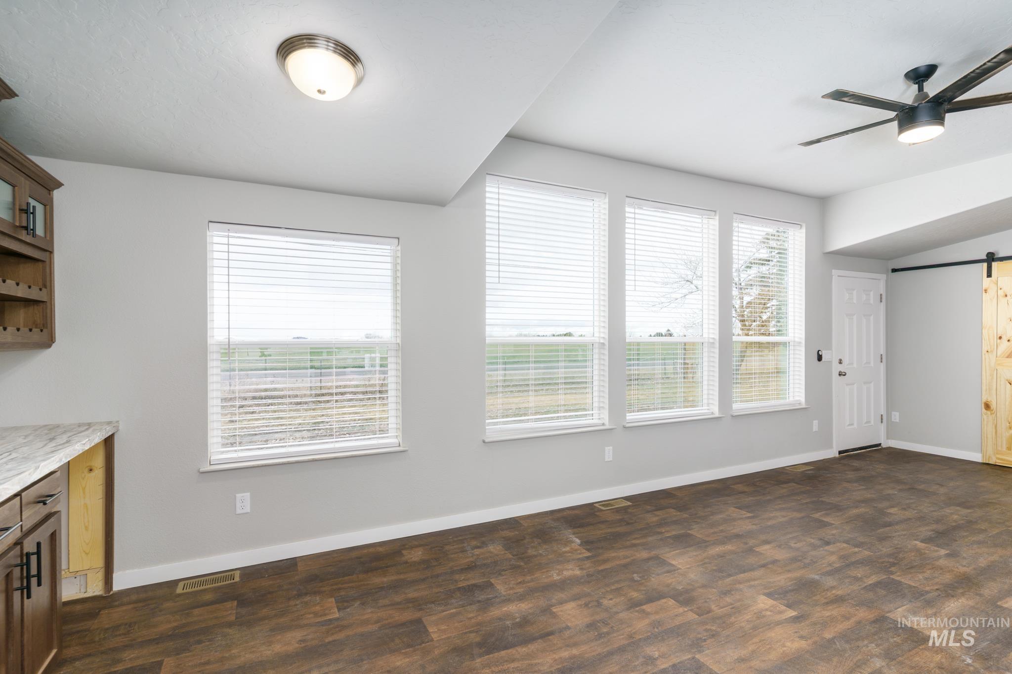 Unfurnished dining area with a barn door, a ceiling fan, and dark wood finished floors
