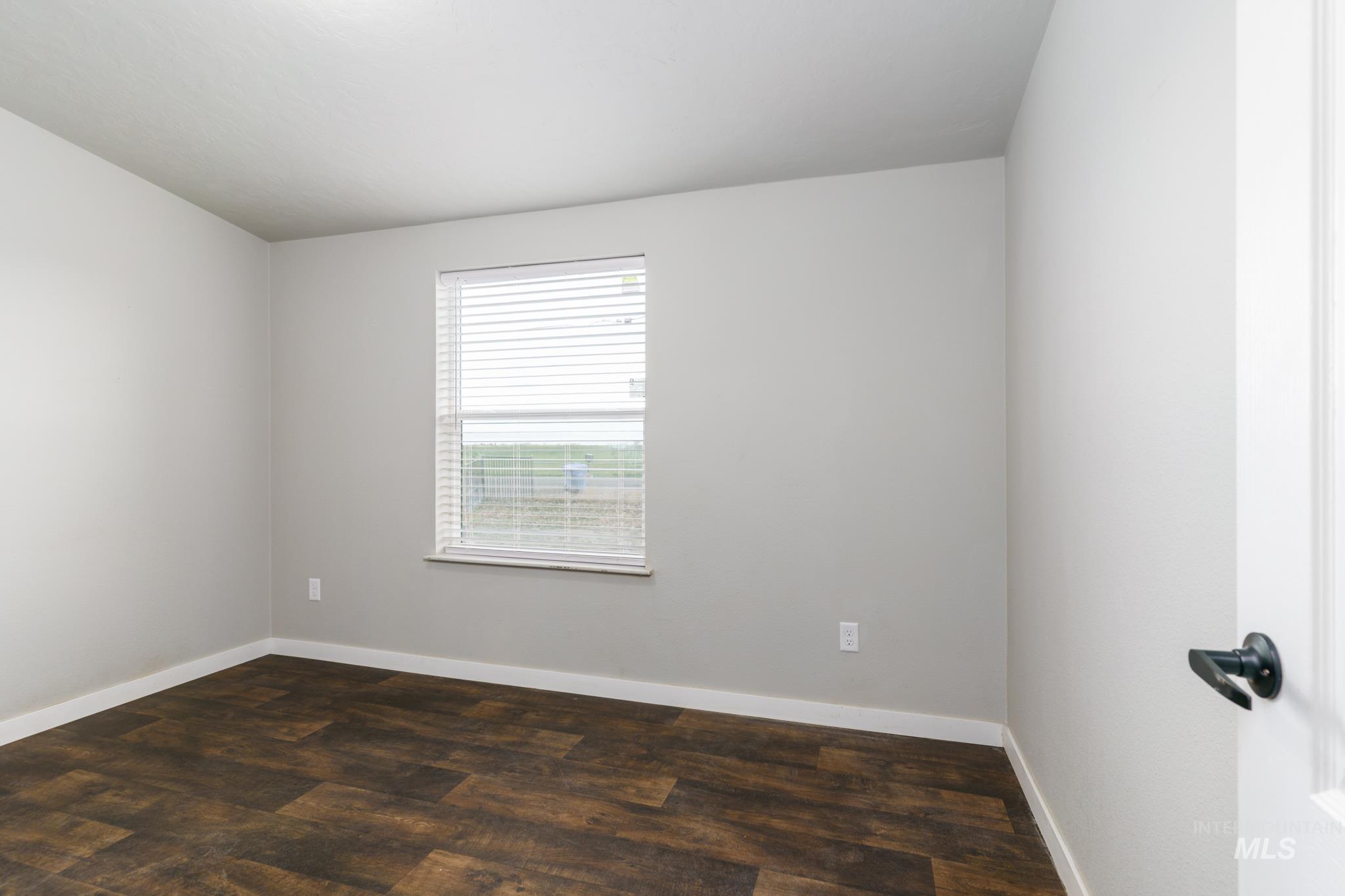 Spare room with dark wood-style flooring and baseboards