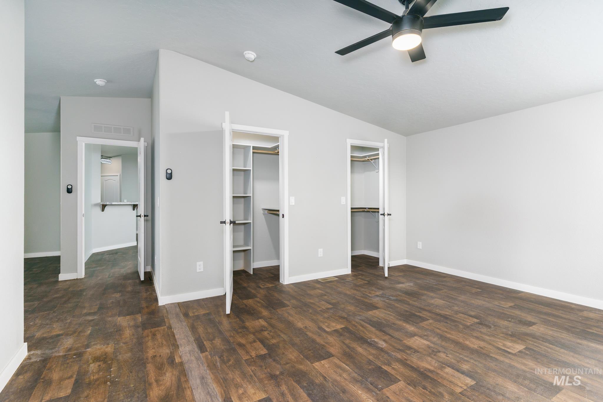 Unfurnished bedroom with multiple closets, dark wood-type flooring, vaulted ceiling, and ceiling fan