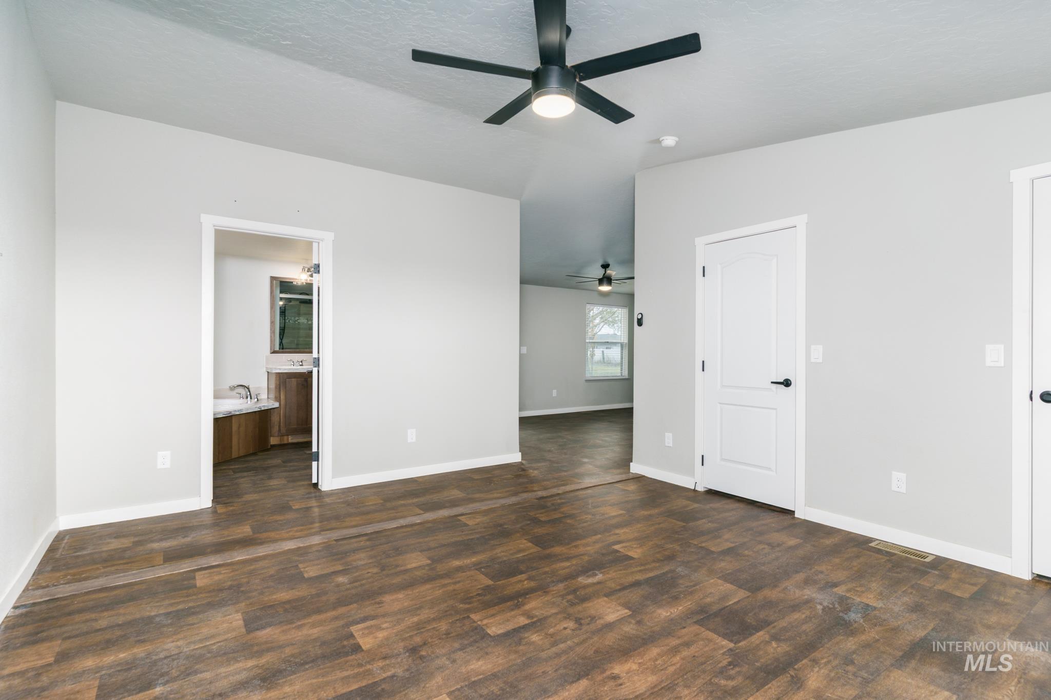 Unfurnished bedroom featuring ensuite bath, dark wood-style flooring, ceiling fan, and a textured ceiling