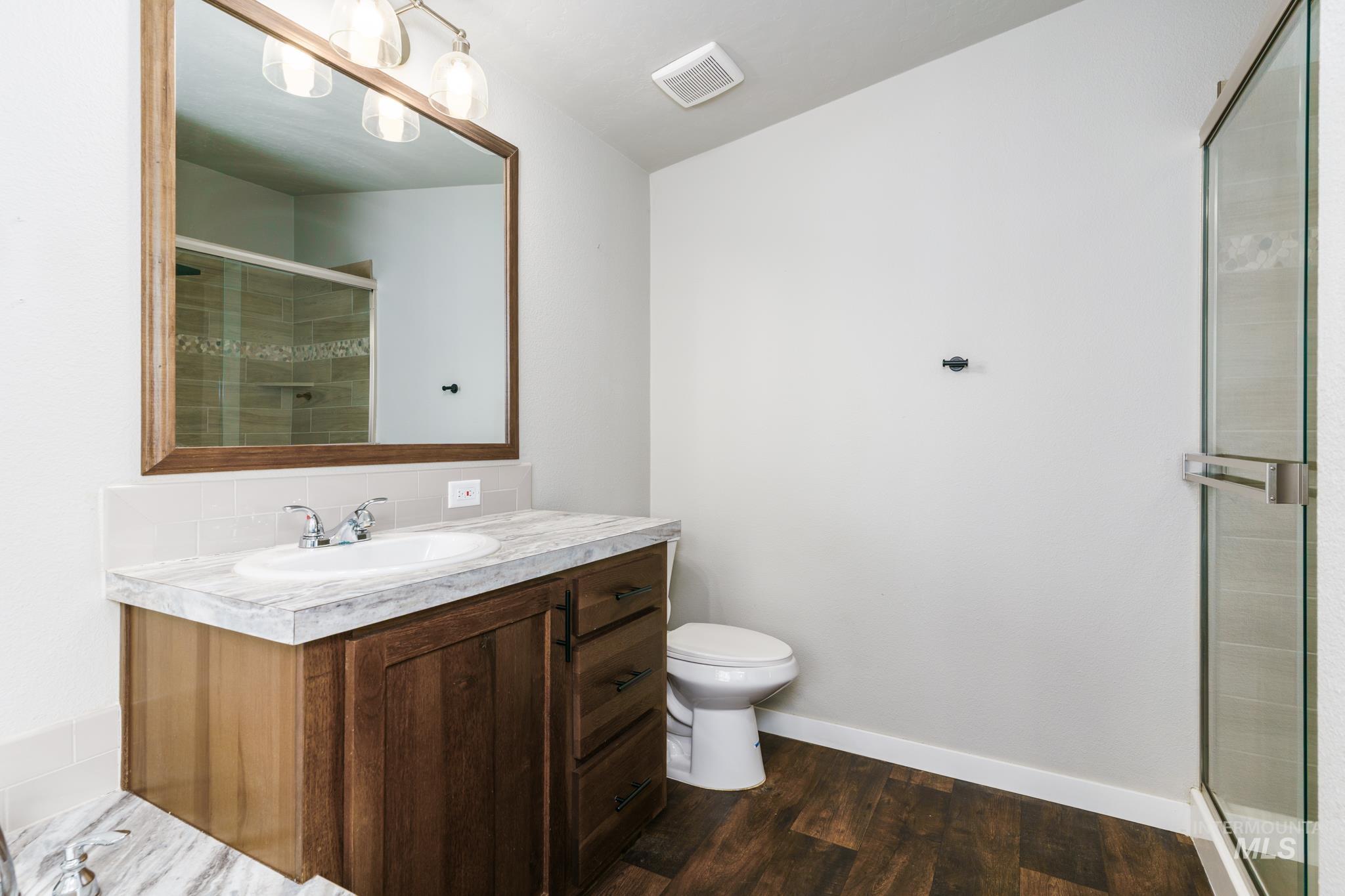 Full bathroom featuring vanity, a stall shower, and dark wood finished floors