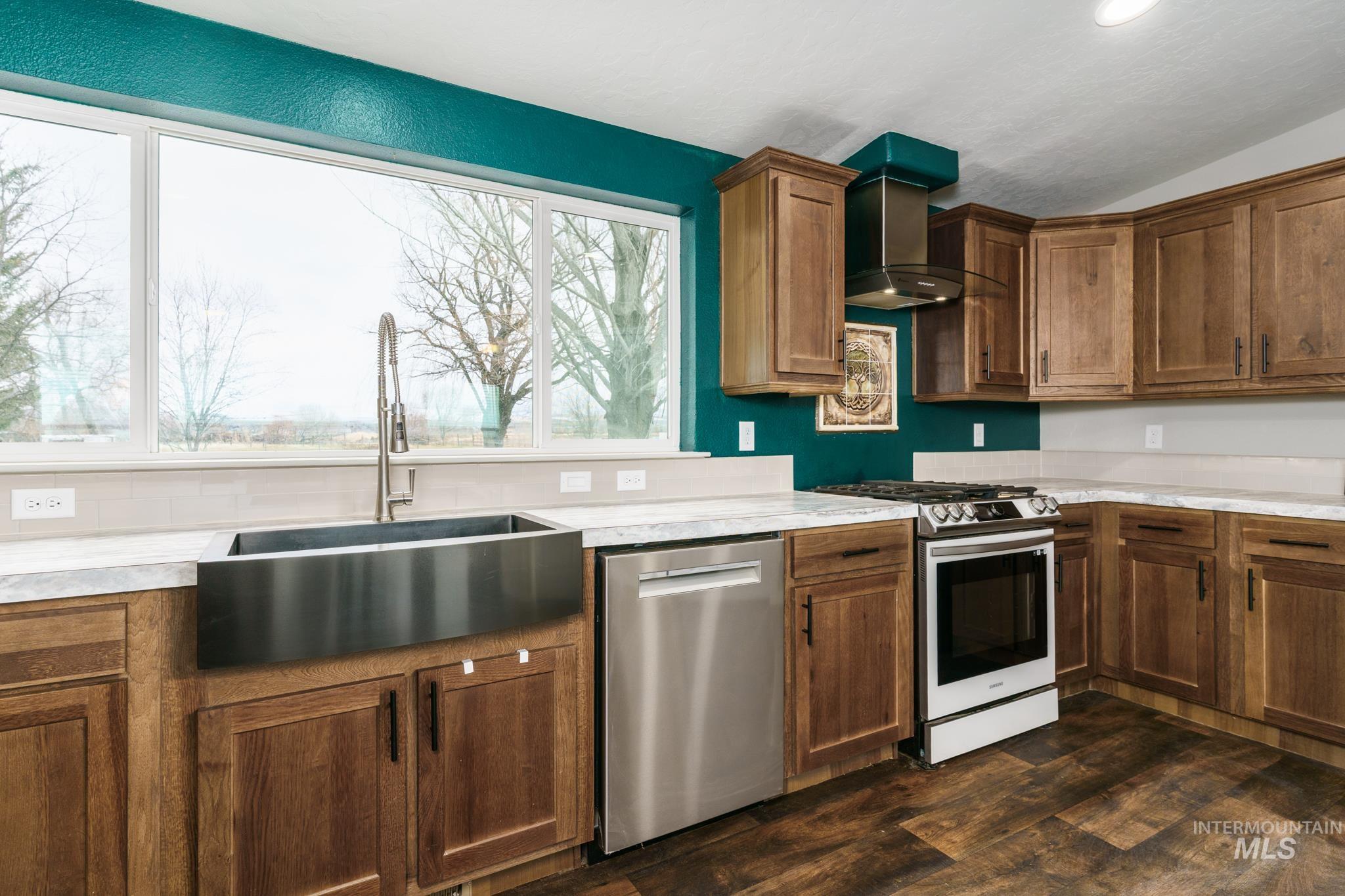 Kitchen featuring appliances with stainless steel finishes, wall chimney range hood, light countertops, lofted ceiling, and dark wood-type flooring