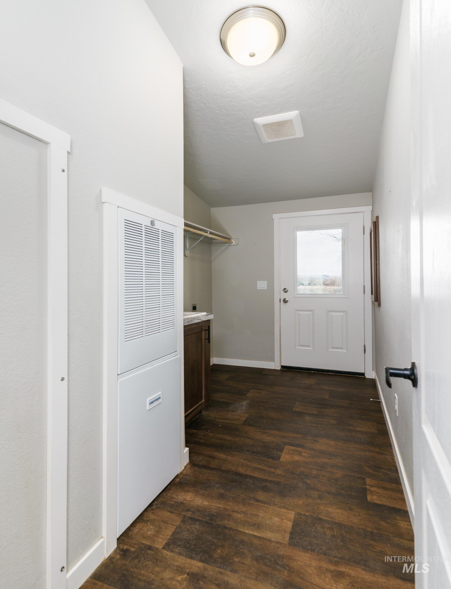 Laundry room featuring a heating unit, dark wood-style flooring, and vaulted ceiling