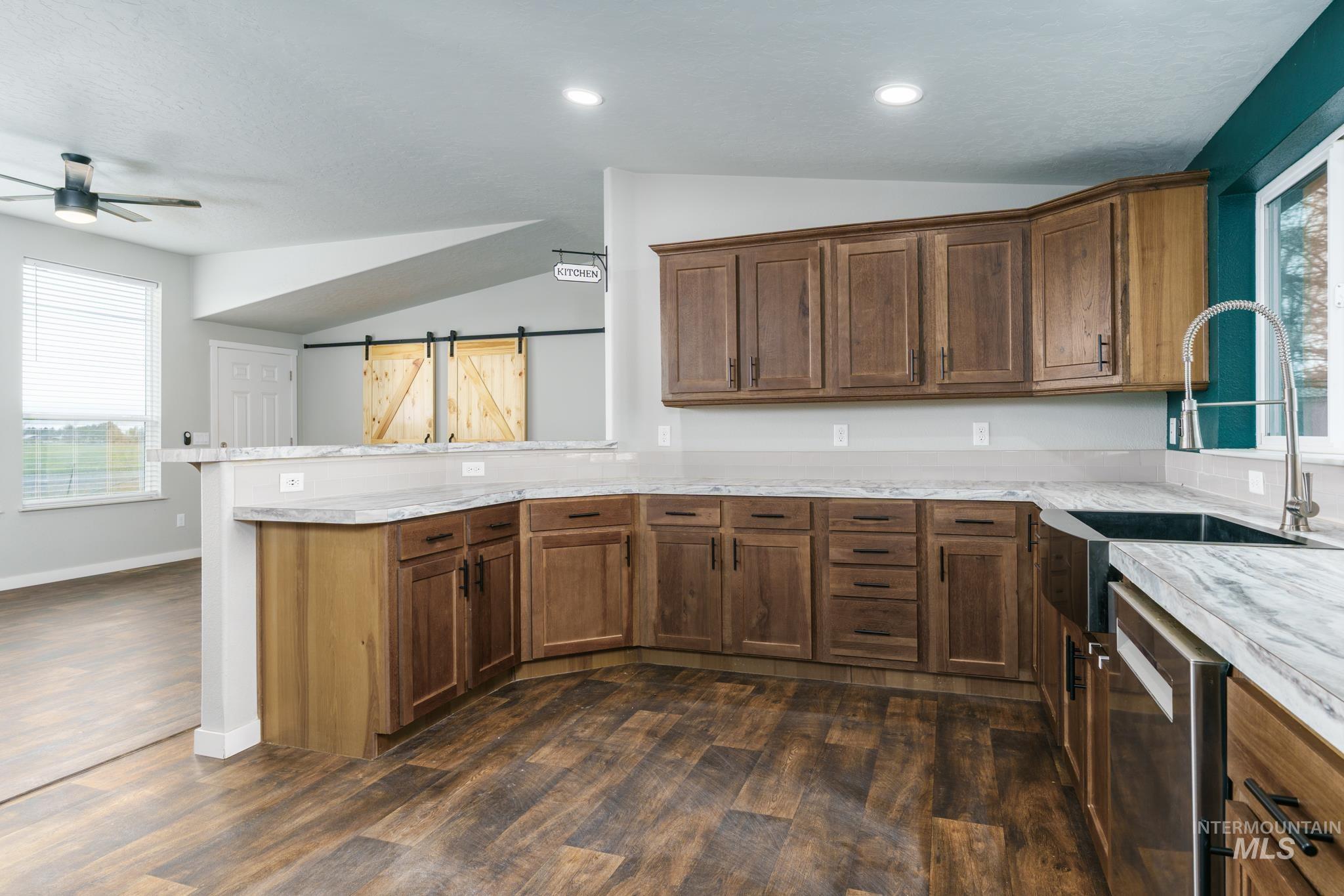 Kitchen featuring healthy amount of natural light, lofted ceiling, dark wood-style floors, a barn door, and dishwasher