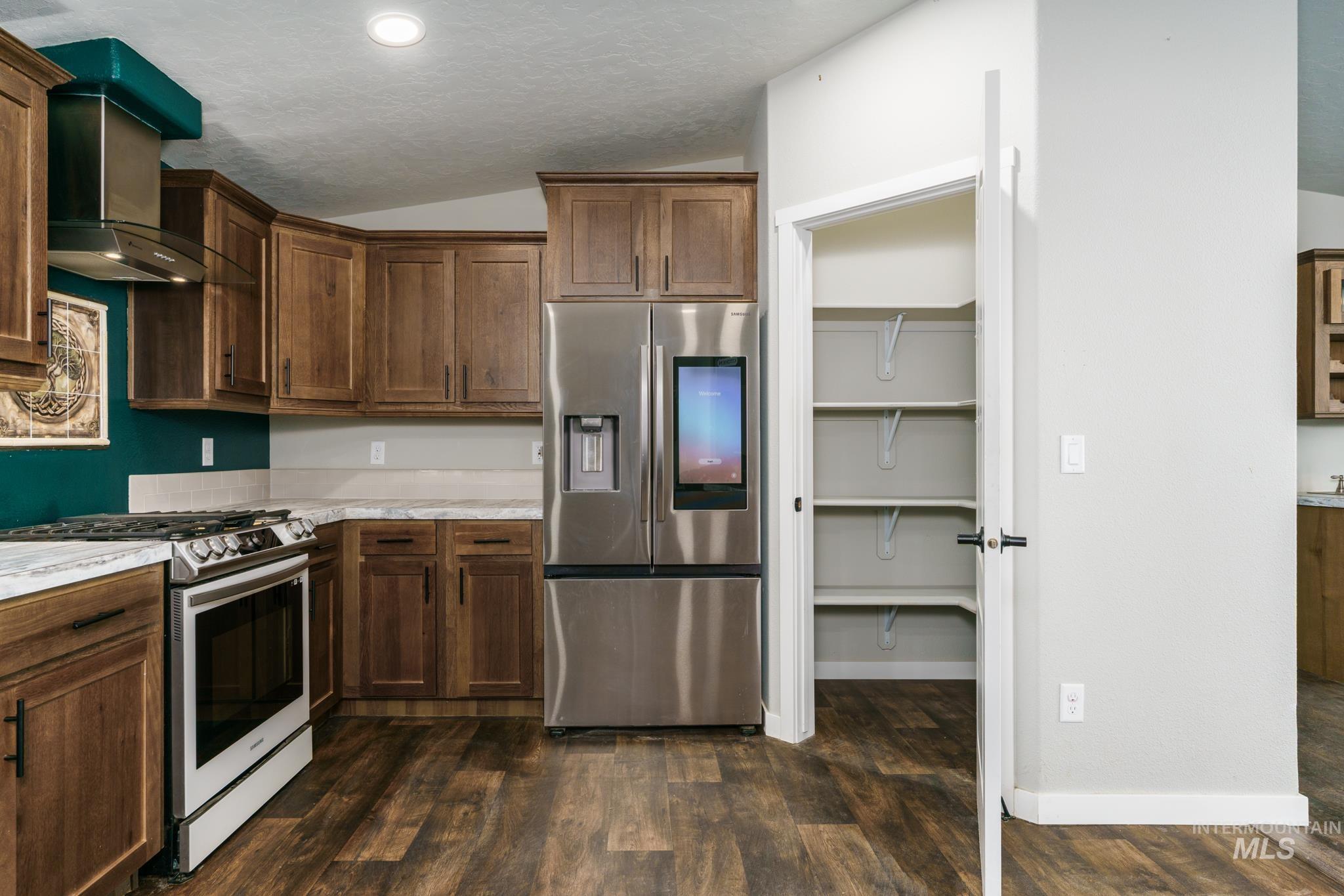 Kitchen featuring vaulted ceiling, appliances with stainless steel finishes, wall chimney exhaust hood, dark wood-style floors, and dark brown cabinets