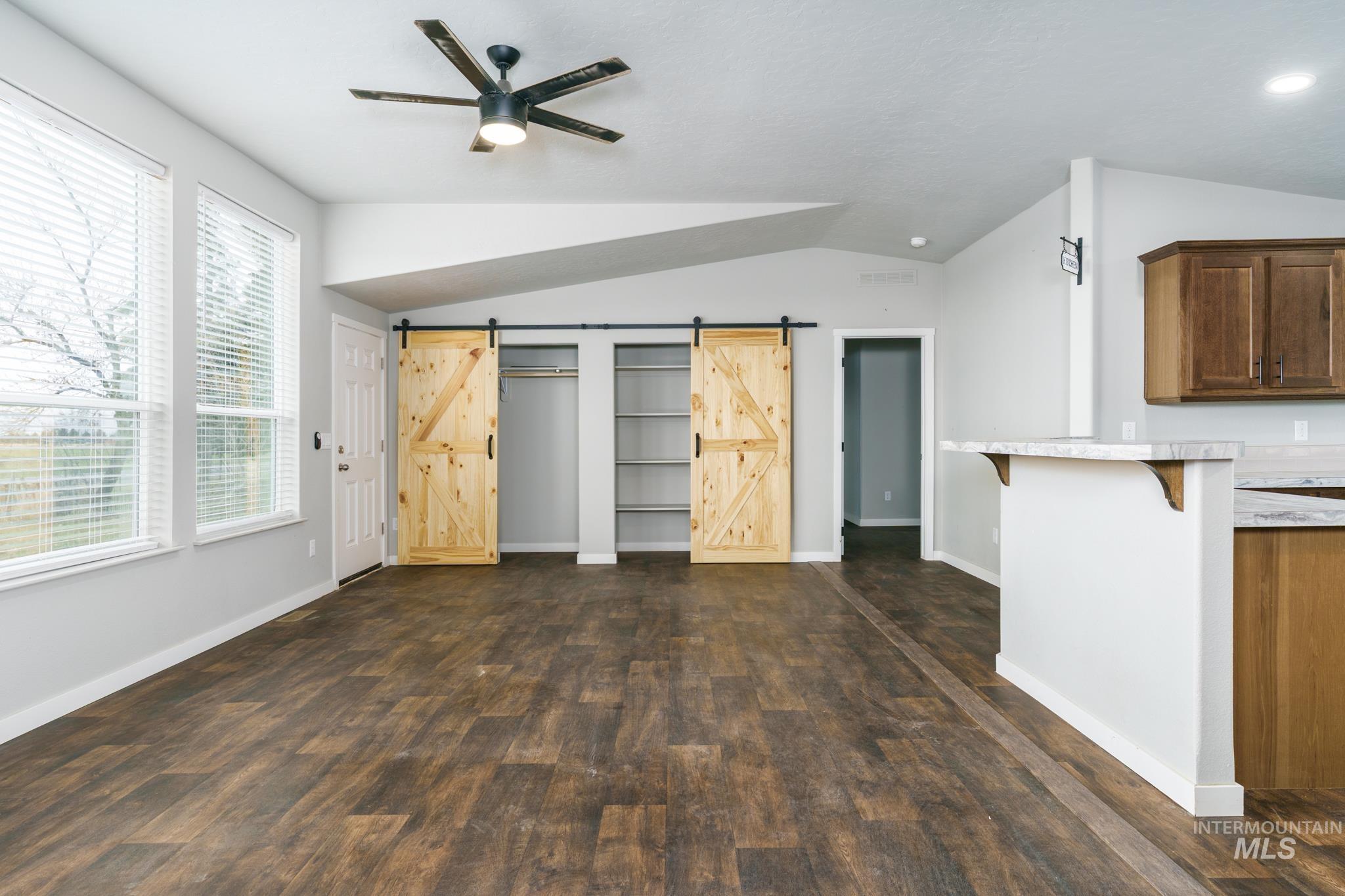 Unfurnished bedroom with dark wood-type flooring, a barn door, vaulted ceiling, and a ceiling fan