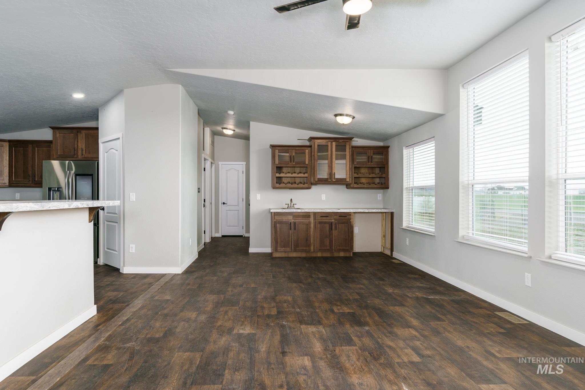 Kitchen with vaulted ceiling, dark wood-style floors, glass insert cabinets, dark brown cabinets, and stainless steel fridge