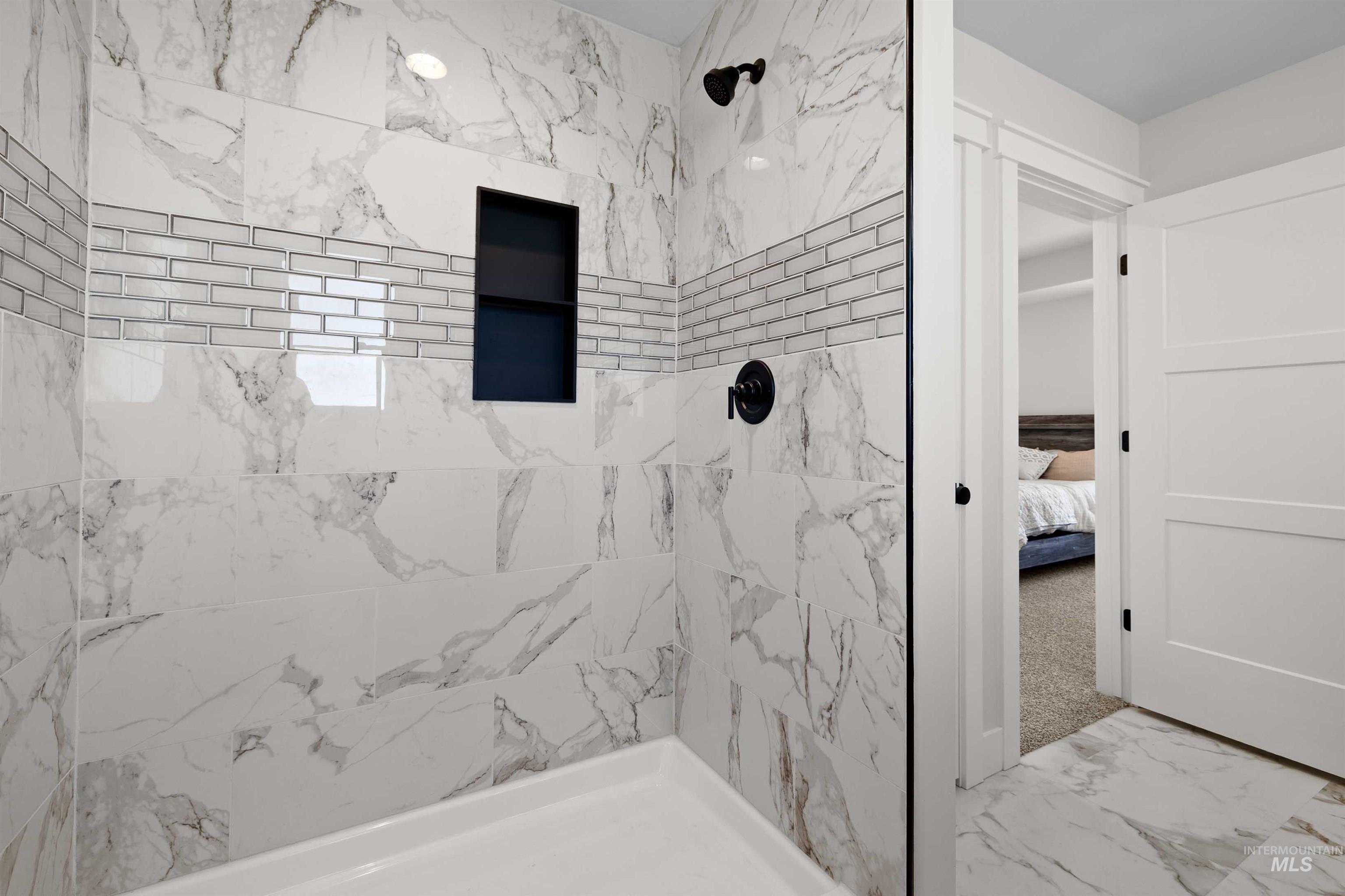 Bathroom featuring a tile shower, marble finish floors, and ensuite bath