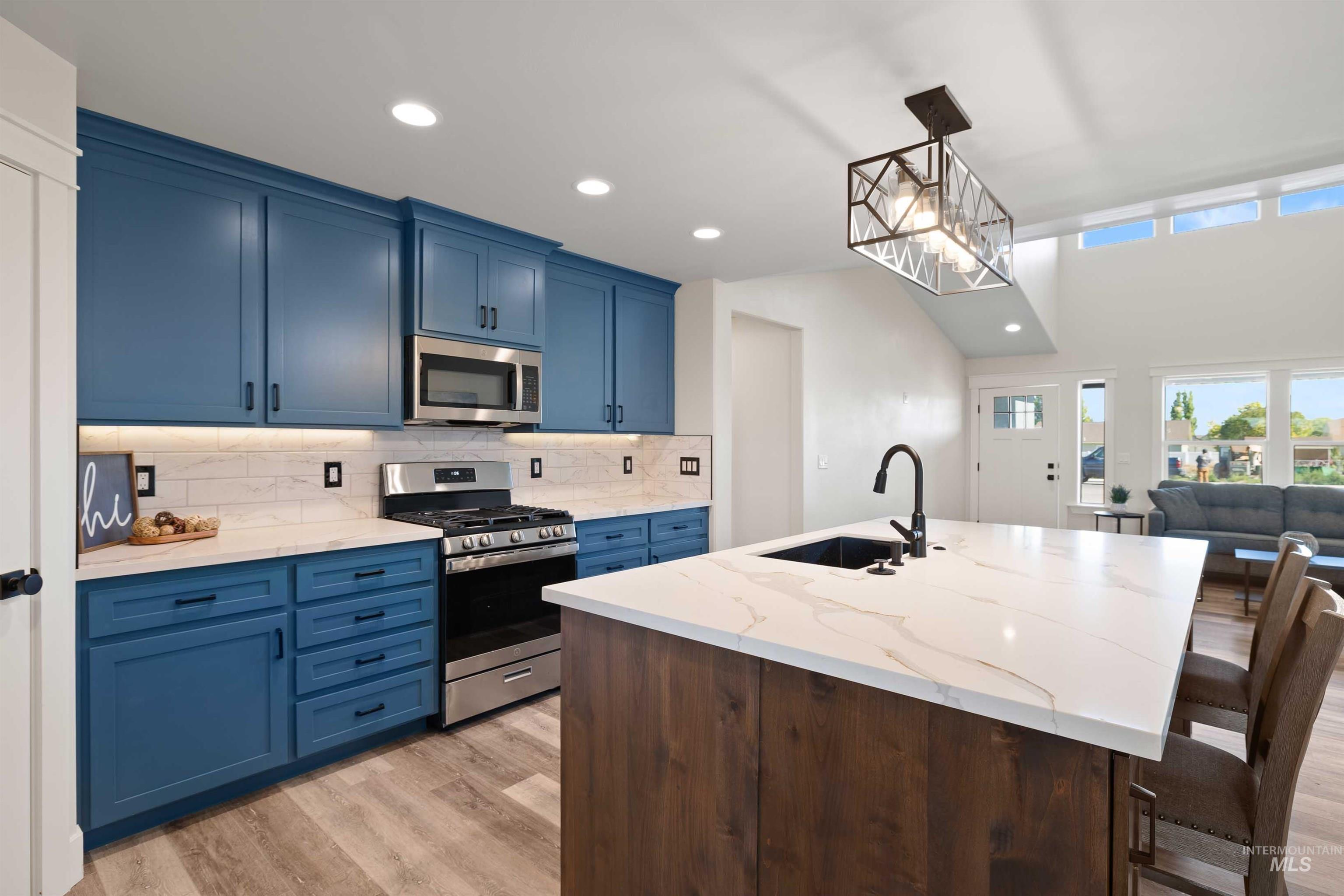 Kitchen featuring appliances with stainless steel finishes, blue cabinetry, light wood-style floors, decorative backsplash, and recessed lighting