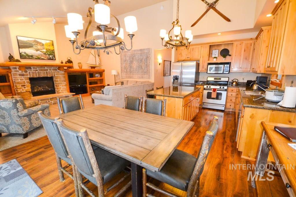 Dining room featuring a chandelier, dark wood-style flooring, a stone fireplace, track lighting, and lofted ceiling