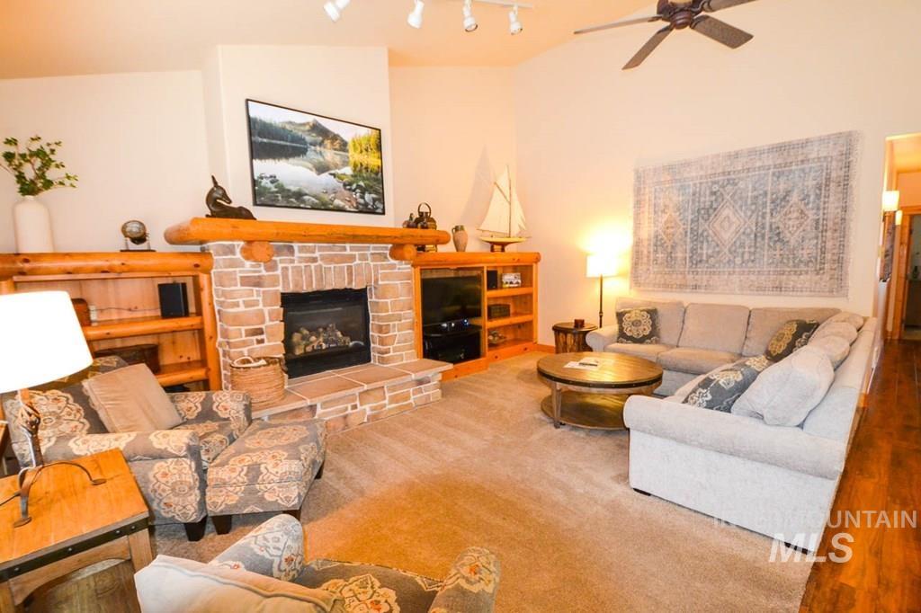 Carpeted living area featuring a fireplace, vaulted ceiling, and a ceiling fan