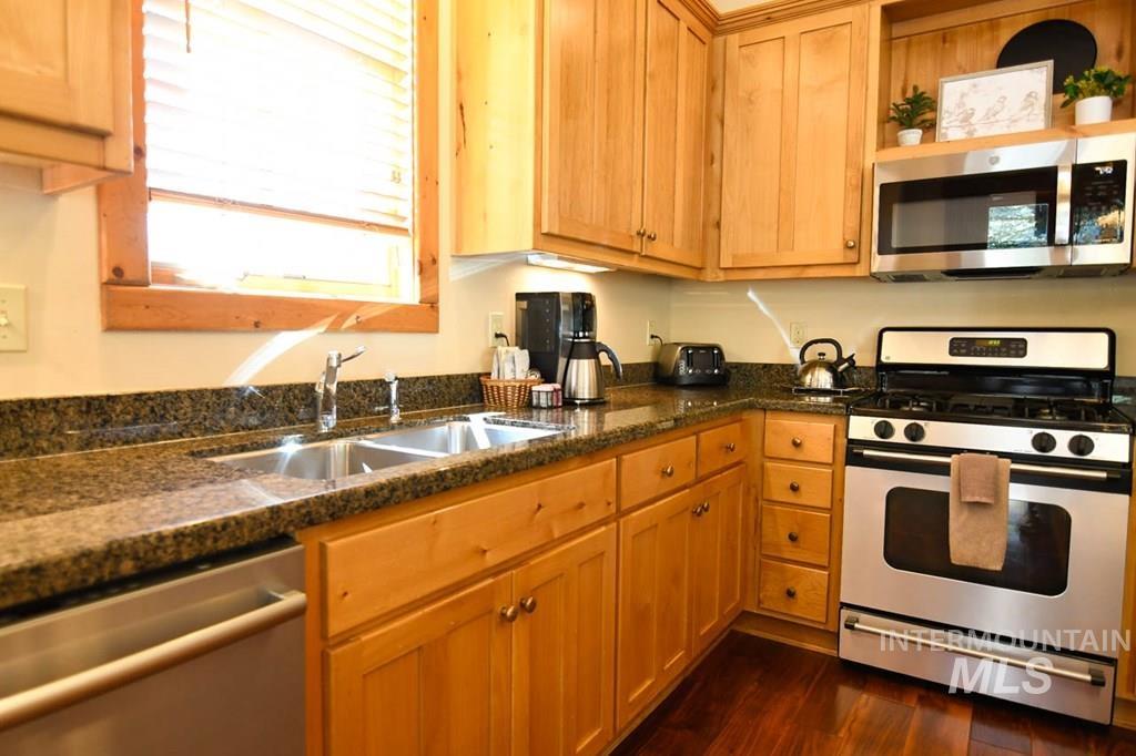 Kitchen with stainless steel appliances, dark stone countertops, dark wood-style floors, and open shelves