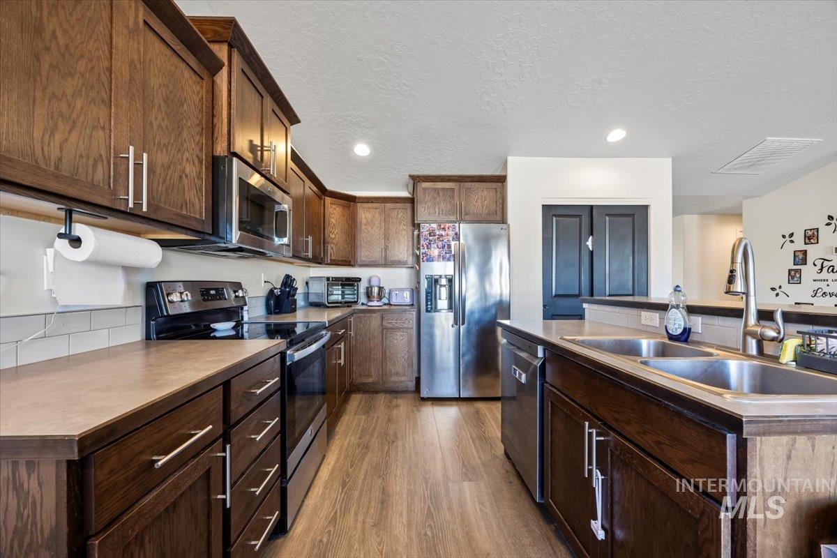 Kitchen with appliances with stainless steel finishes, wood finished floors, recessed lighting, a textured ceiling, and dark brown cabinets