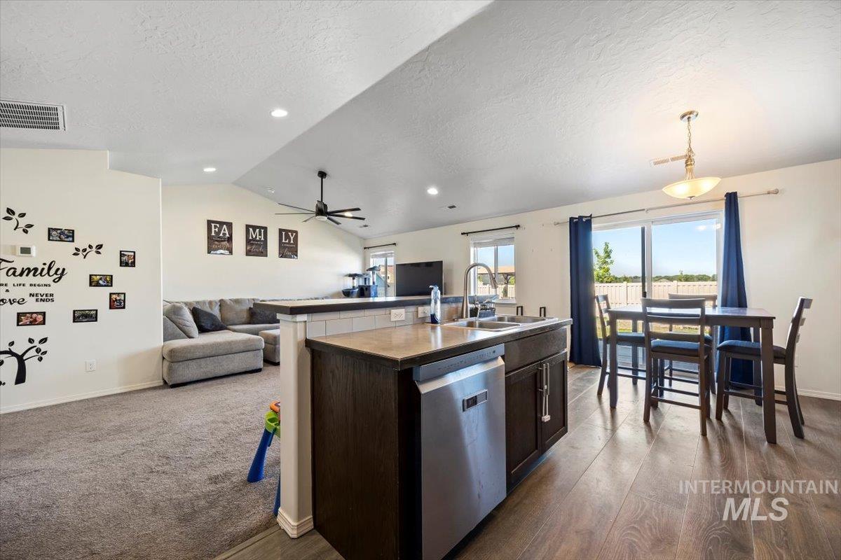 Kitchen featuring open floor plan, stainless steel dishwasher, a textured ceiling, vaulted ceiling, and an island with sink