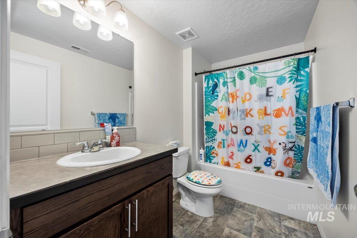Bathroom featuring vanity, a textured ceiling, shower / bathtub combination with curtain, and stone finish floors