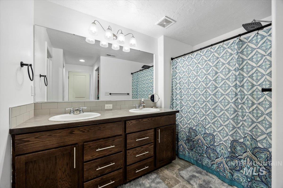 Full bath with double vanity, a textured ceiling, a shower with curtain, and decorative backsplash