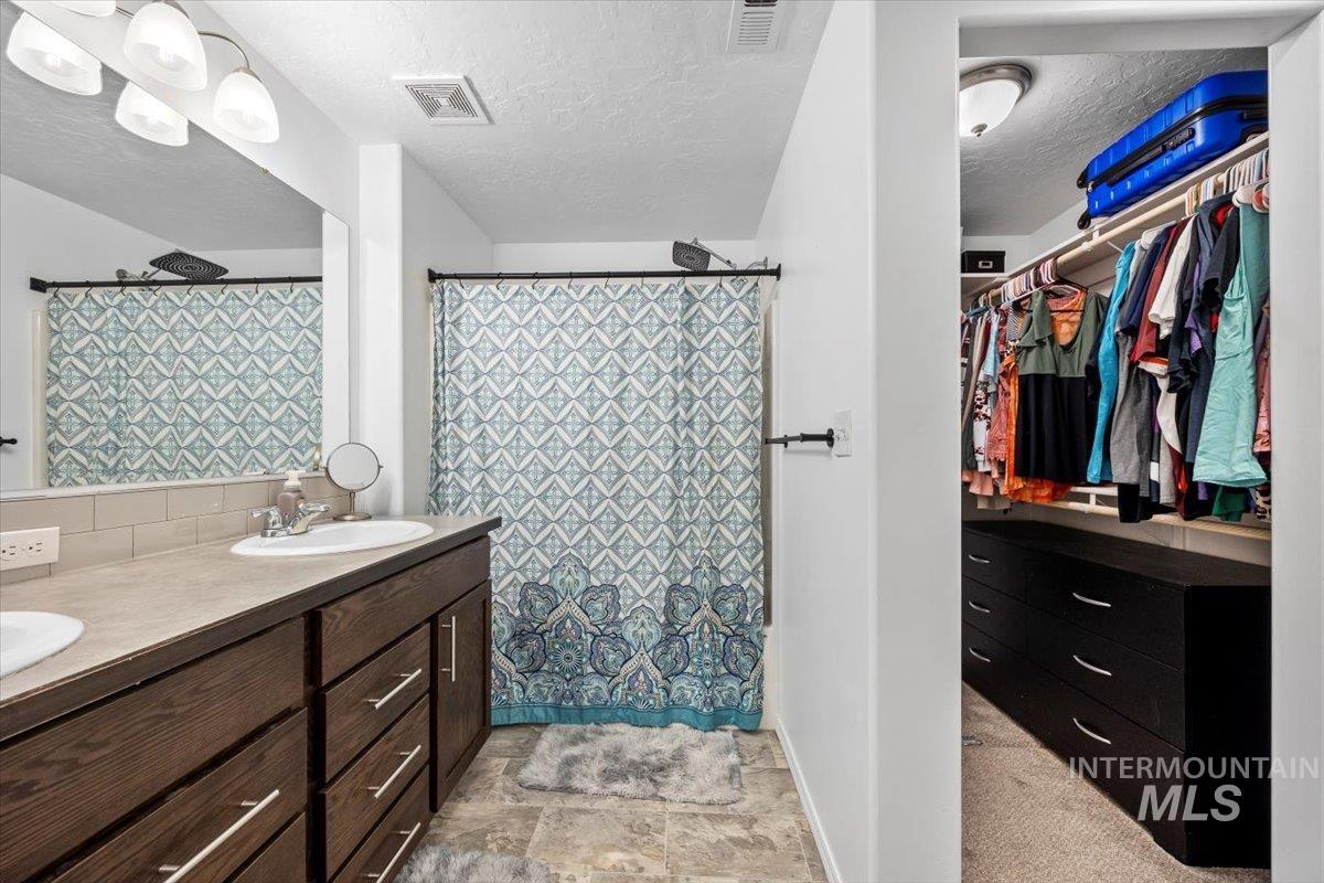 Bathroom with a textured ceiling, double vanity, a shower with curtain, and a walk in closet