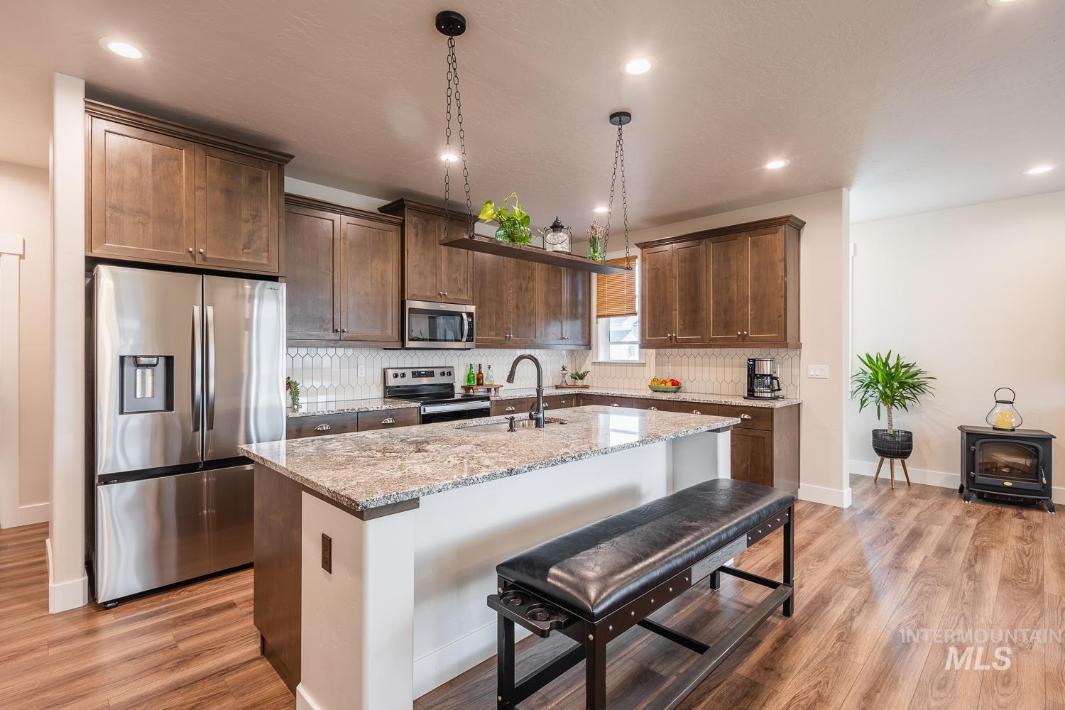 Kitchen with appliances with stainless steel finishes, light stone countertops, a breakfast bar, a kitchen island with sink, and hanging light fixtures