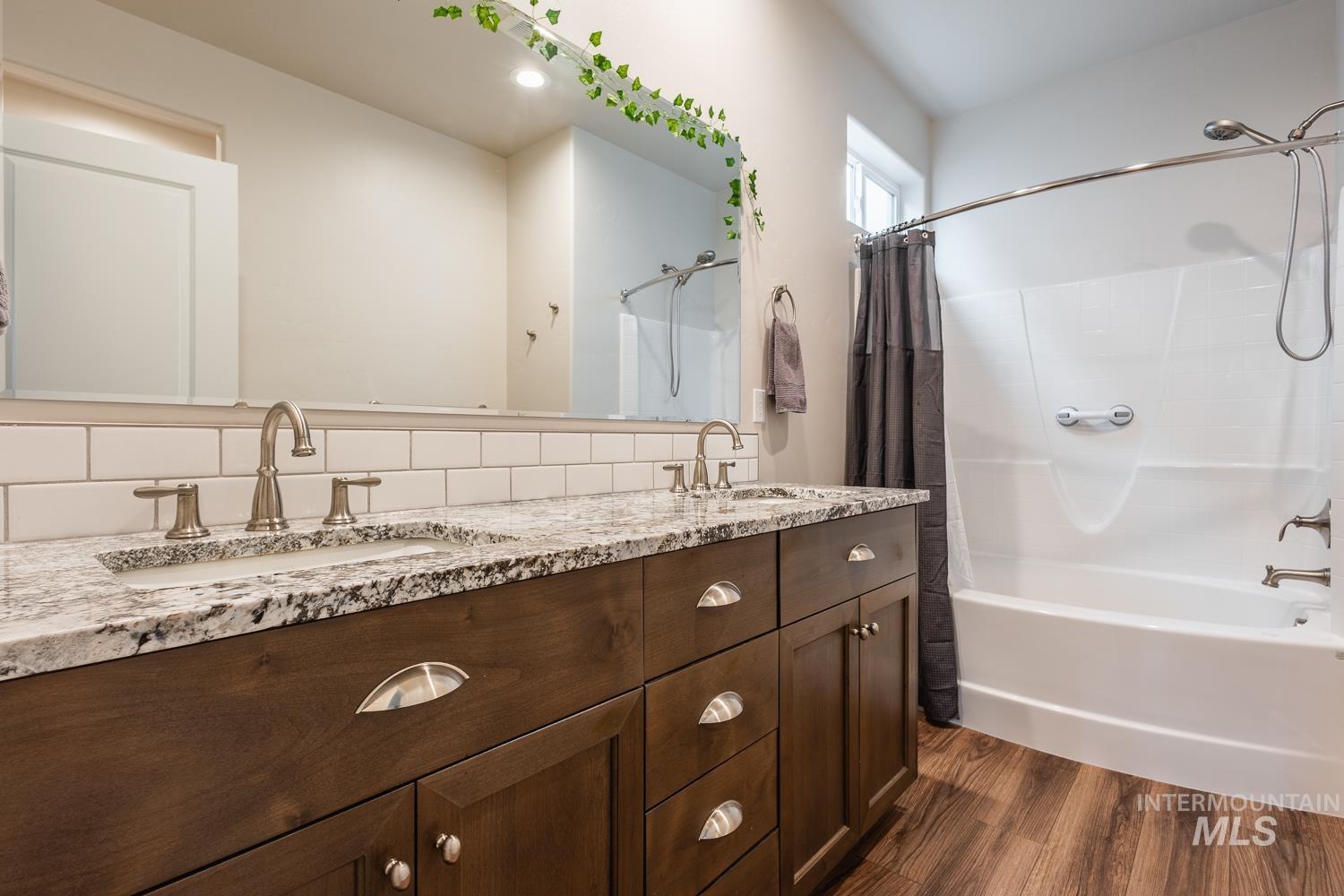 Bathroom with shower / tub combo with curtain, double vanity, dark wood-style floors, and tasteful backsplash