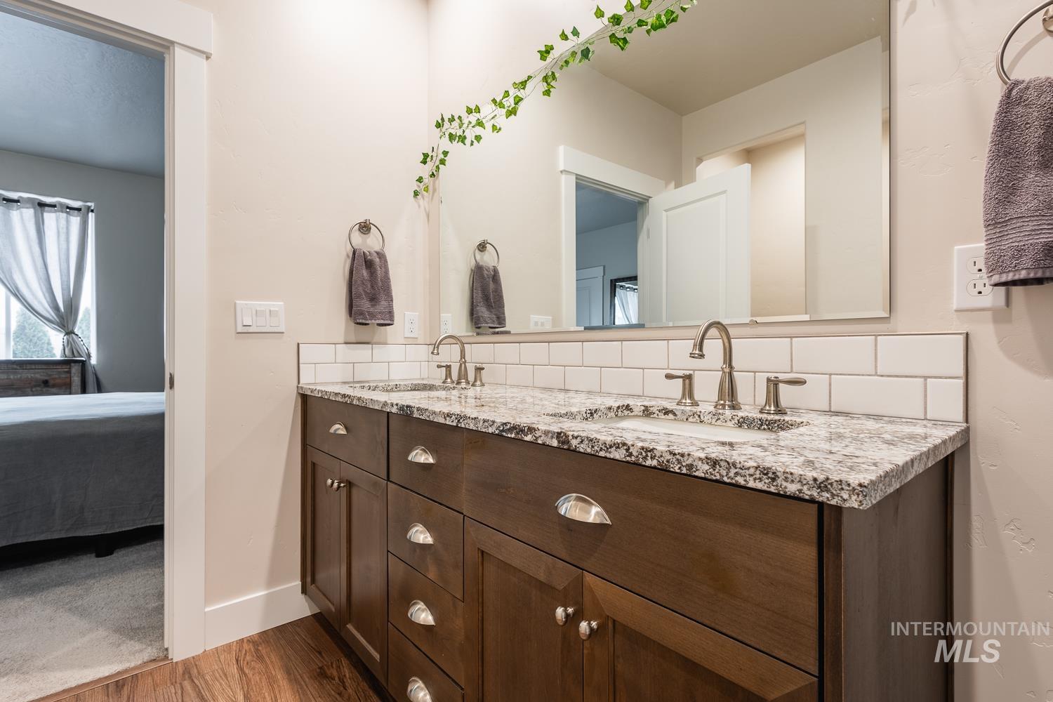 Bathroom with double vanity, connected bathroom, dark wood finished floors, and backsplash