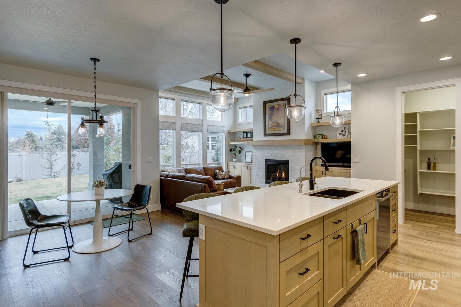 Kitchen with a warm lit fireplace, an island with sink, light wood finished floors, open floor plan, and decorative light fixtures