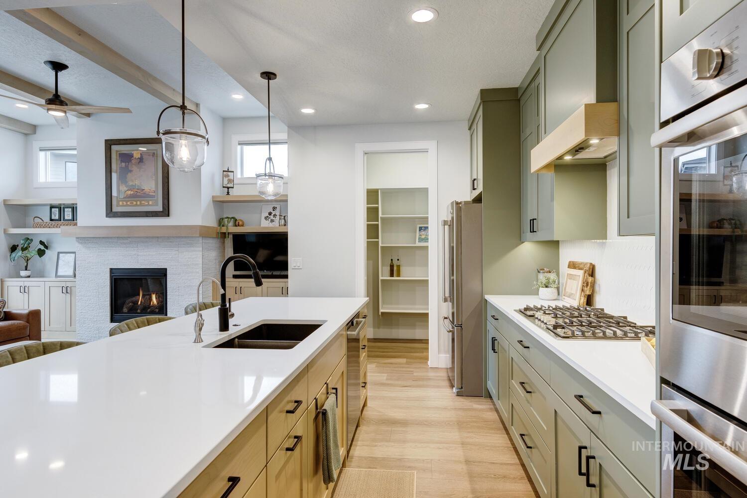 Kitchen with appliances with stainless steel finishes, open floor plan, decorative light fixtures, light wood-style floors, and beamed ceiling