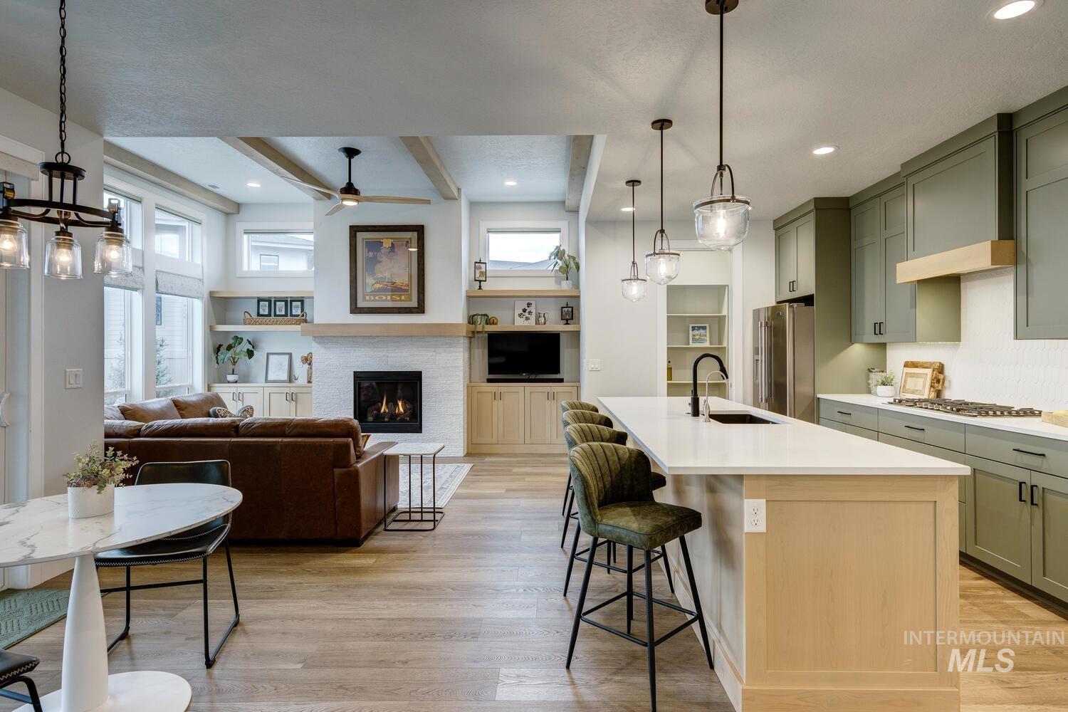 Kitchen featuring open floor plan, pendant lighting, green cabinets, a kitchen island with sink, and beamed ceiling