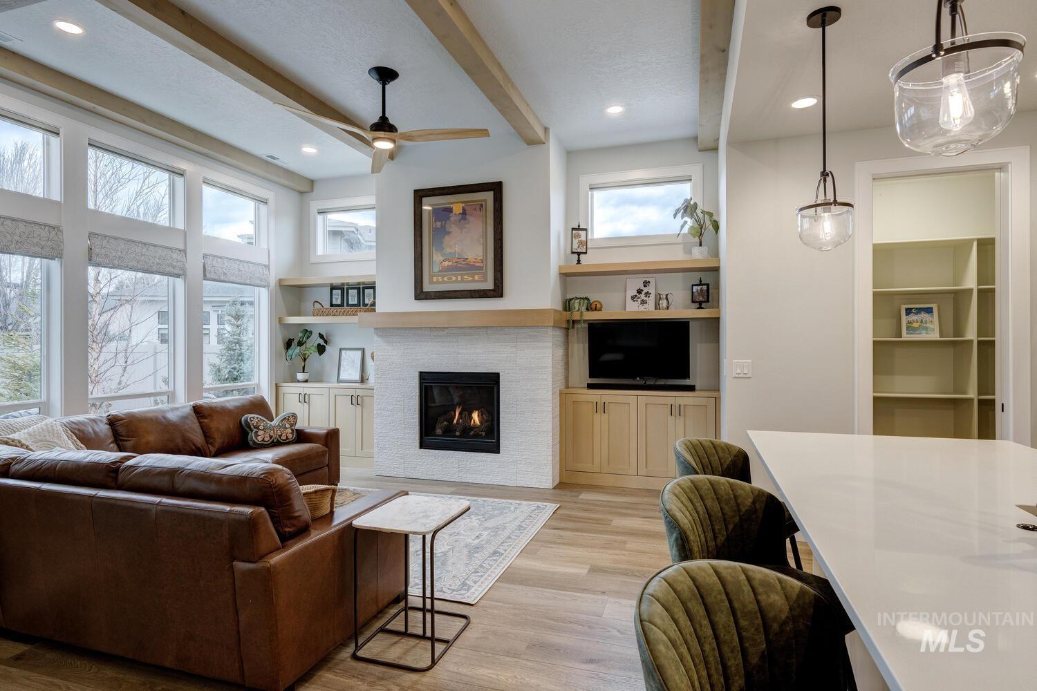 Living room with beam ceiling, light wood-style floors, a glass covered fireplace, built in shelves, and plenty of natural light