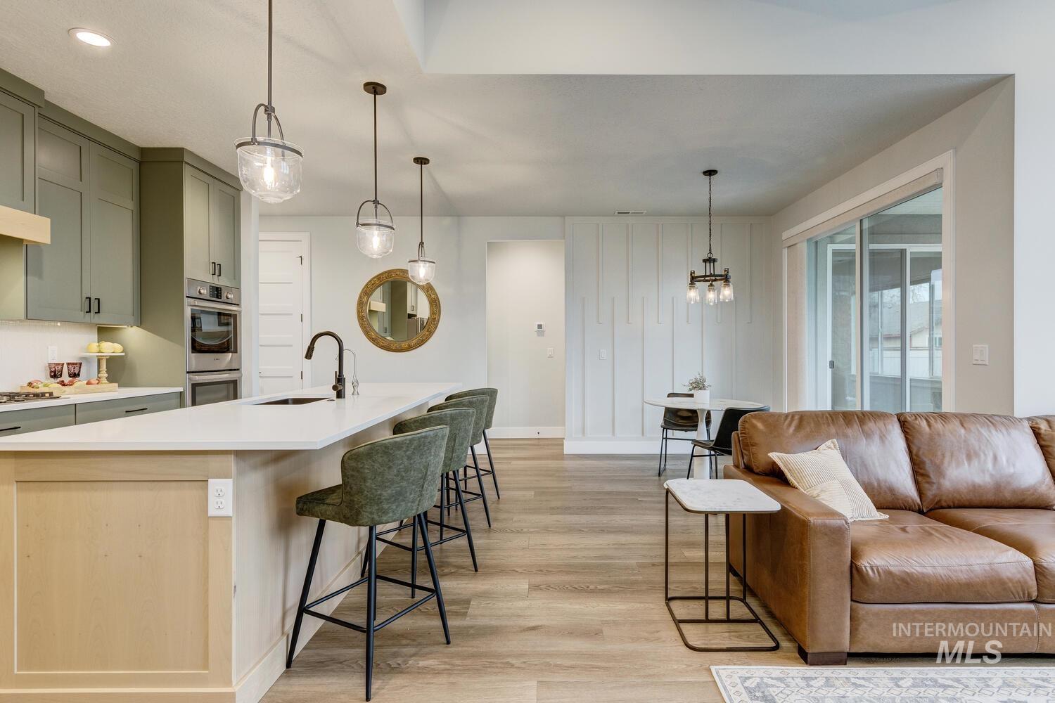 Kitchen featuring pendant lighting, a breakfast bar, light wood-style flooring, stainless steel double oven, and a kitchen island with sink