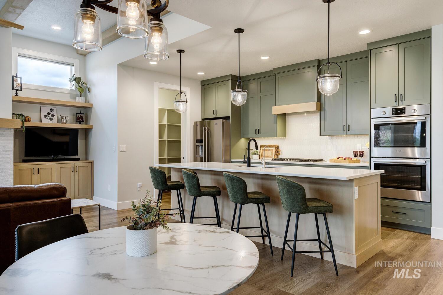 Kitchen featuring green cabinets, stainless steel appliances, a kitchen bar, an island with sink, and backsplash