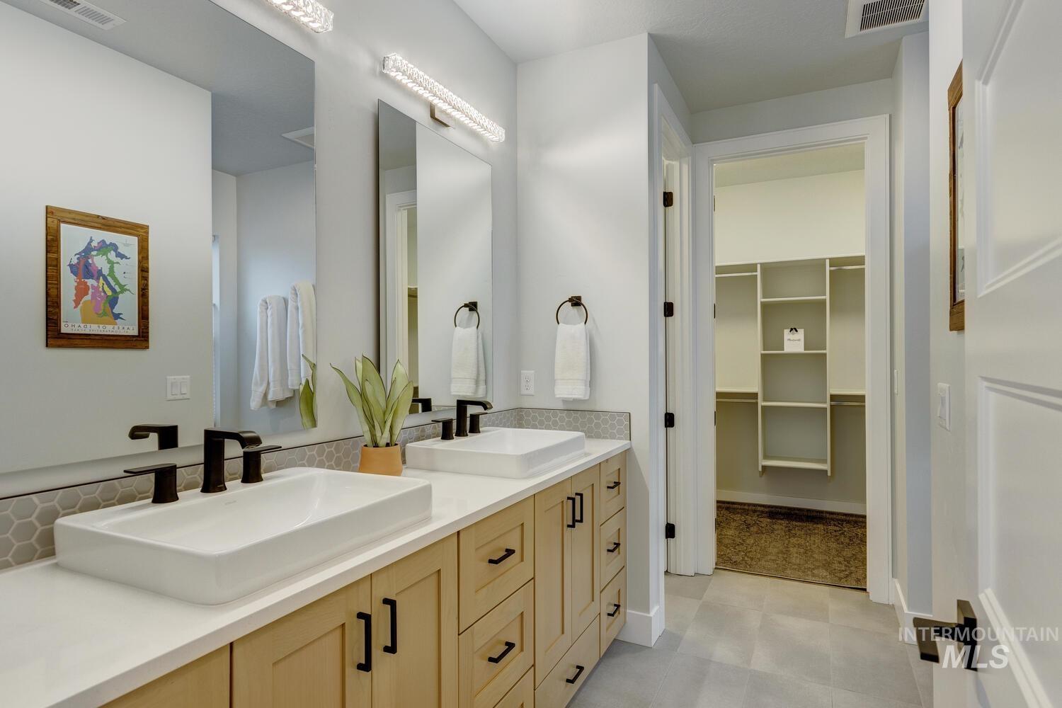 Bathroom with double vanity, a spacious closet, and light flooring