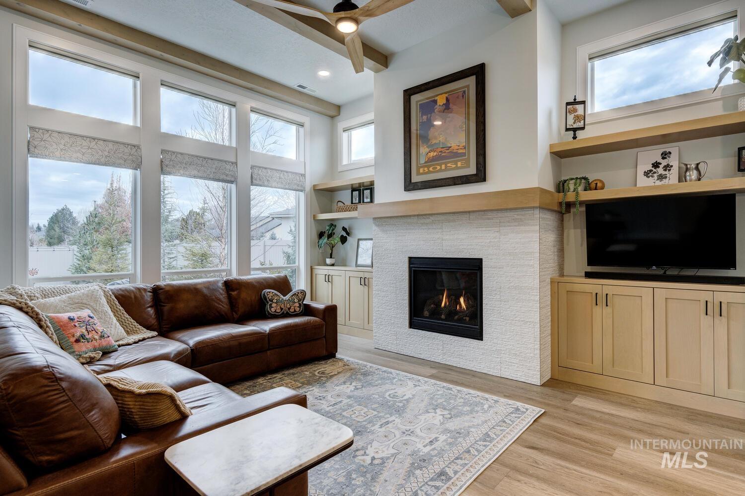 Living room featuring light wood-type flooring, ceiling fan, built in features, and a fireplace