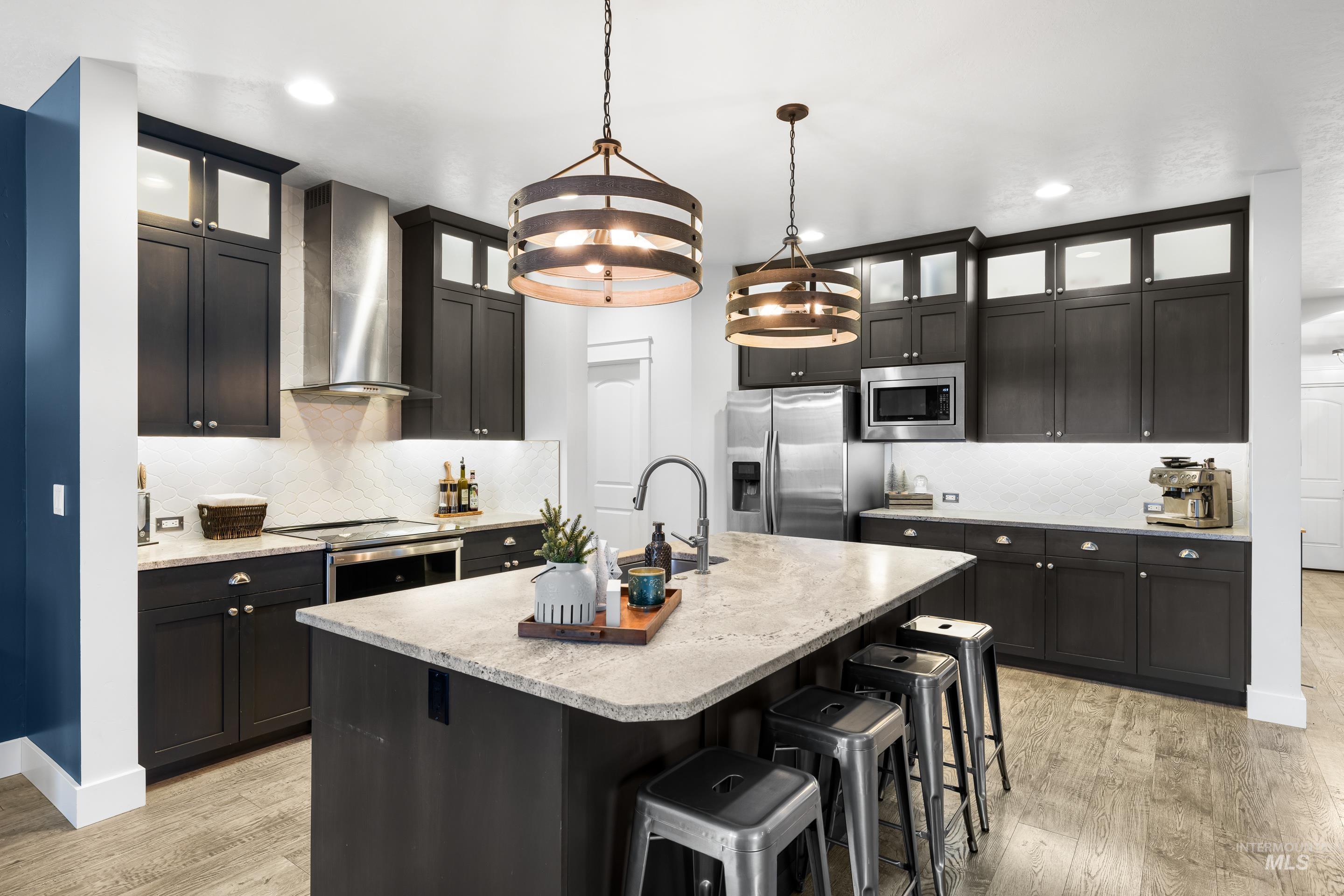 Kitchen with hanging light fixtures, stainless steel appliances, a kitchen breakfast bar, glass insert cabinets, and a center island with sink
