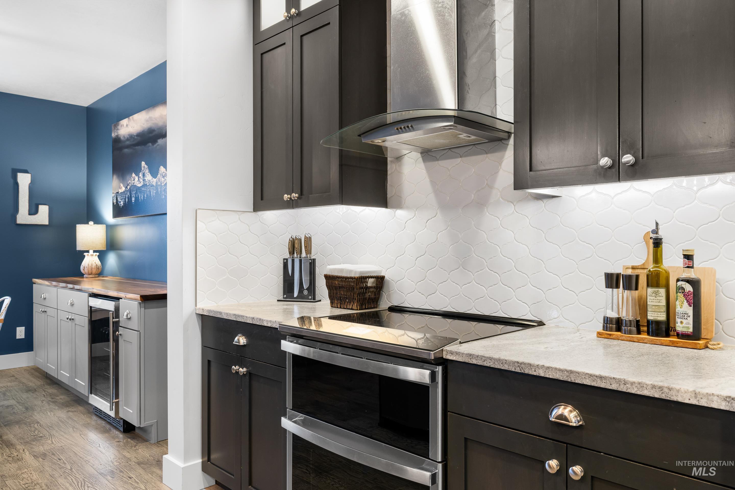 Kitchen with wall chimney range hood, range with two ovens, glass insert cabinets, tasteful backsplash, and beverage cooler
