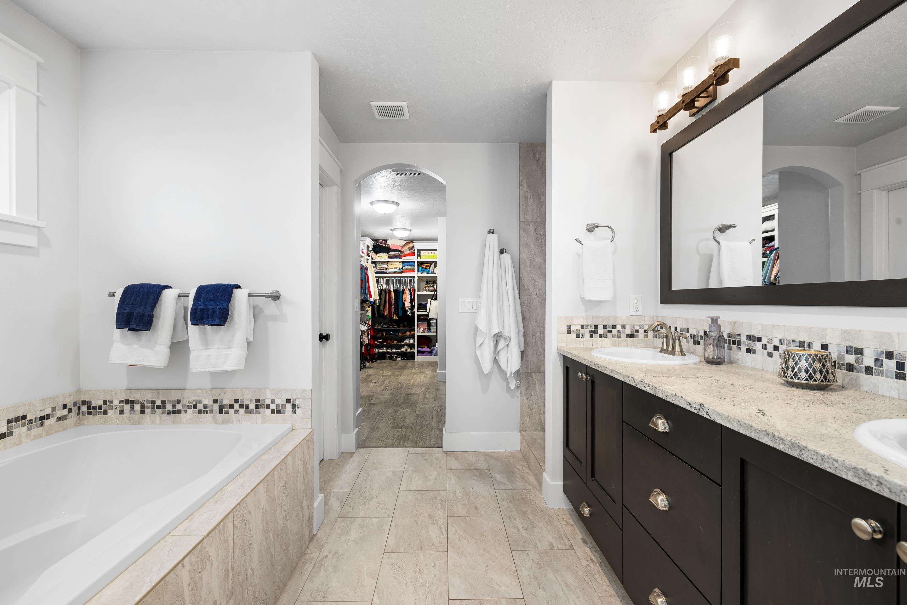 Bathroom featuring a walk in closet, double vanity, a garden tub, and decorative backsplash
