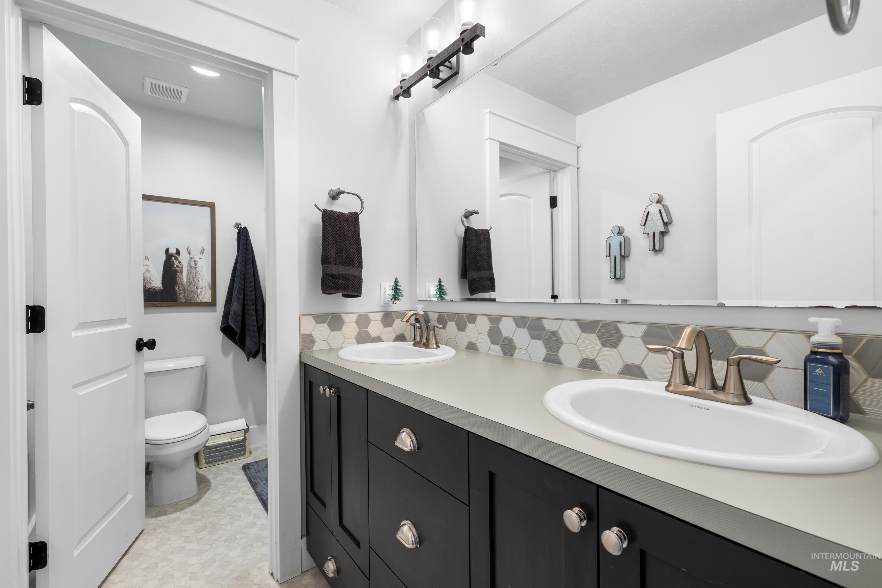Bathroom featuring double vanity, tasteful backsplash, and light floors