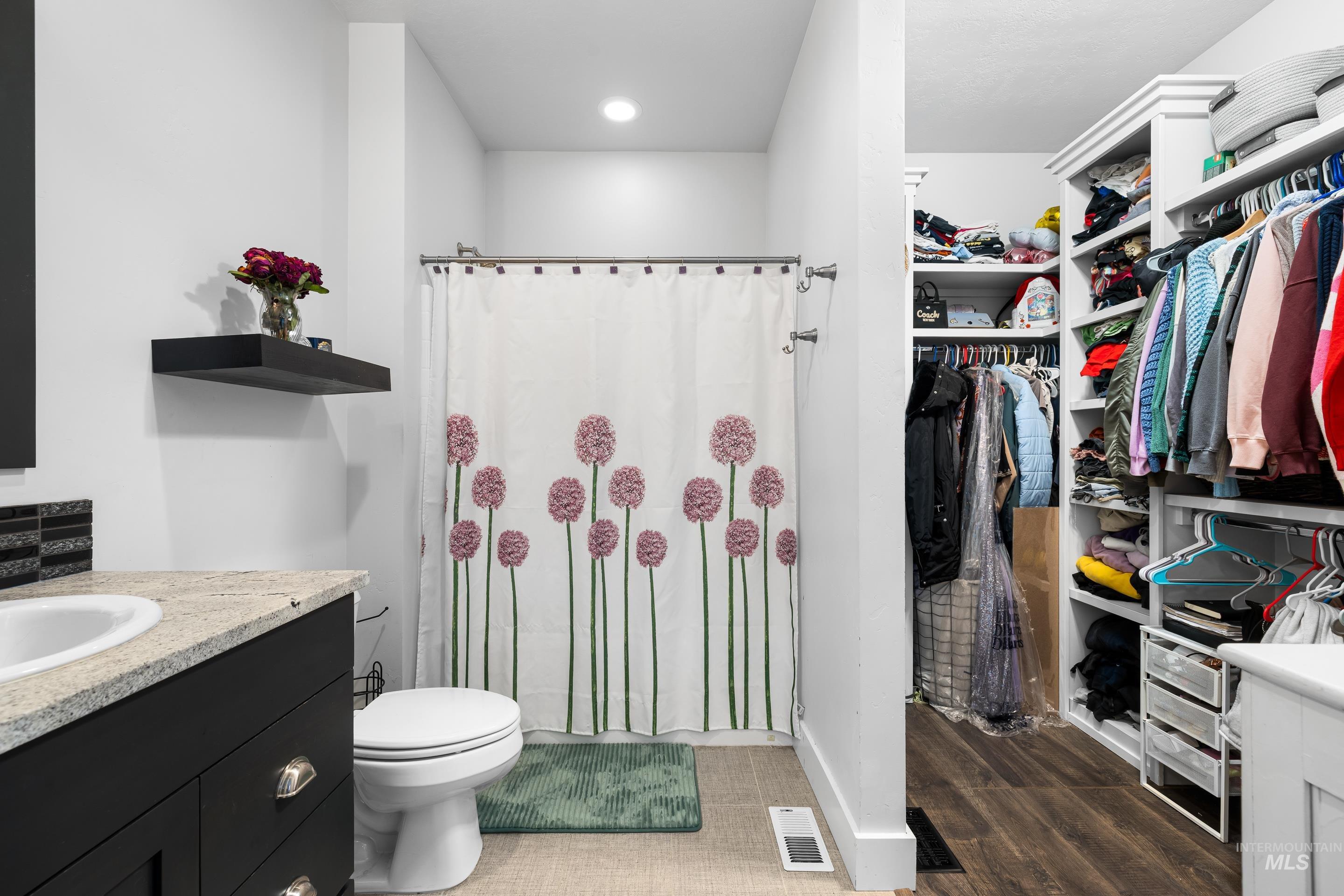 Full bath featuring vanity, a stall shower, a spacious closet, and dark wood finished floors