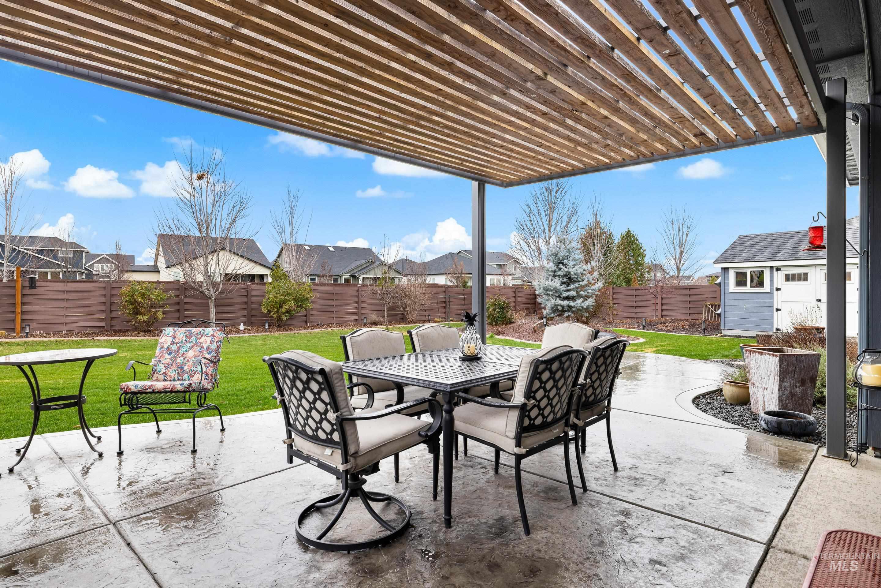 Fenced backyard featuring a pergola, outdoor dining area, a patio area, an outbuilding, and a residential view
