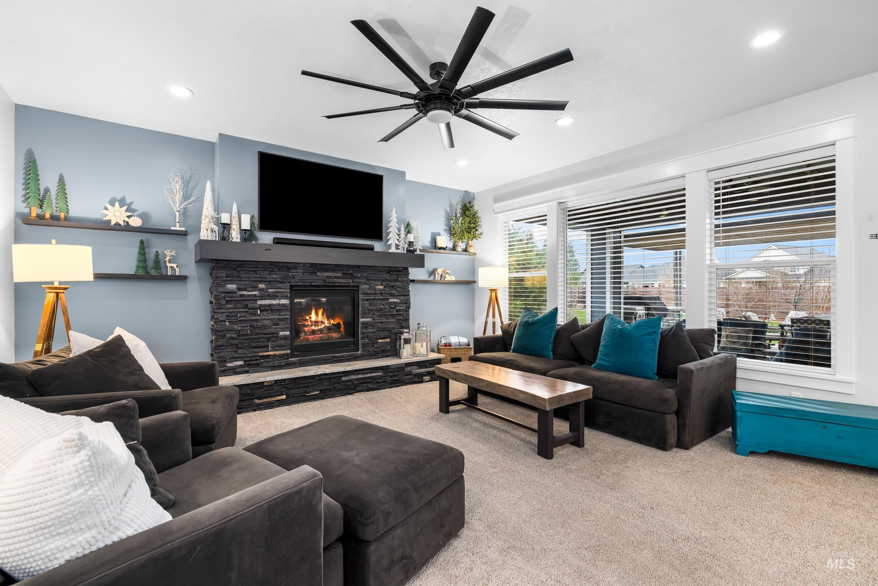 Living area featuring light carpet, ceiling fan, and a stone fireplace