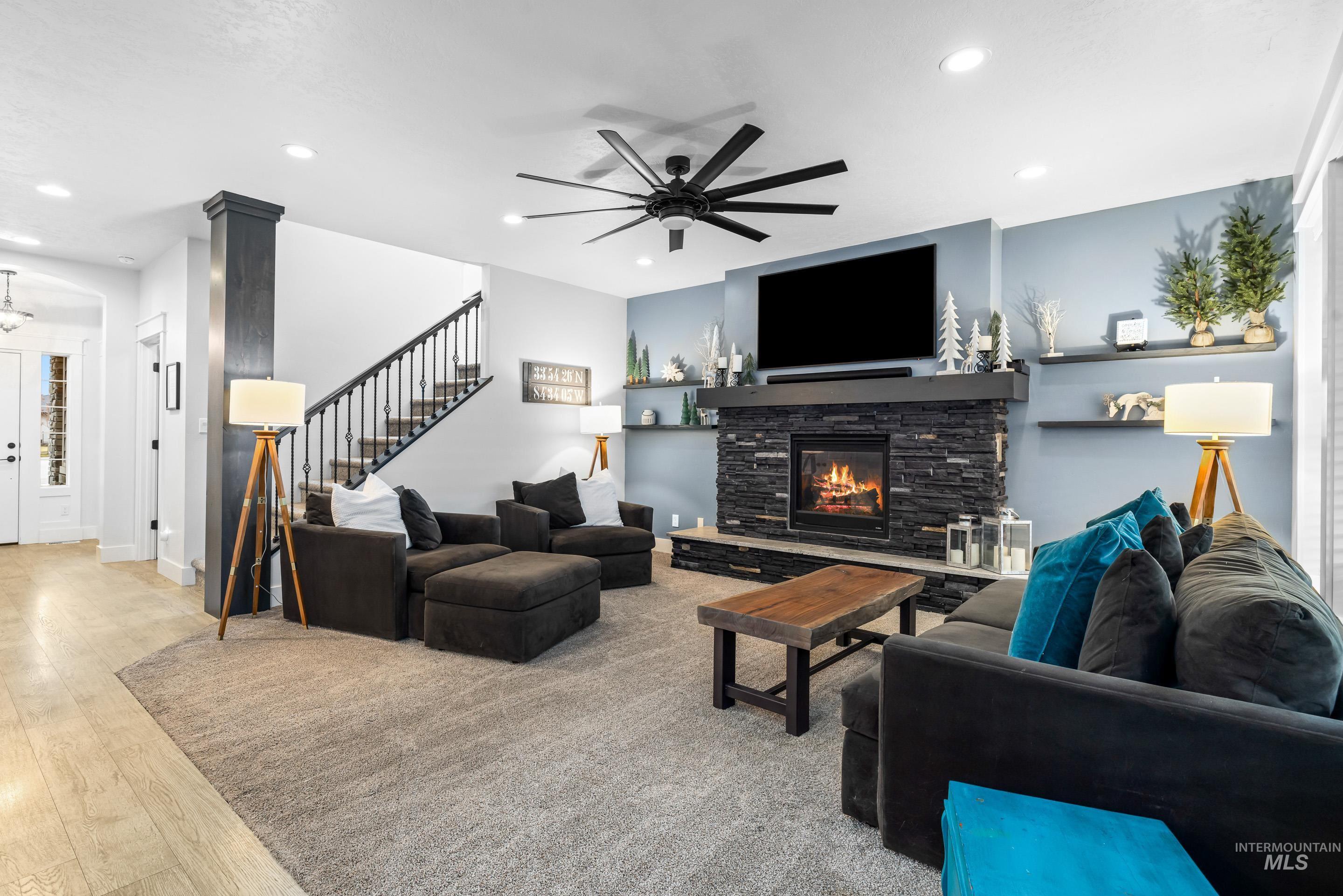 Living area featuring light wood finished floors, stairs, ceiling fan, a stone fireplace, and recessed lighting