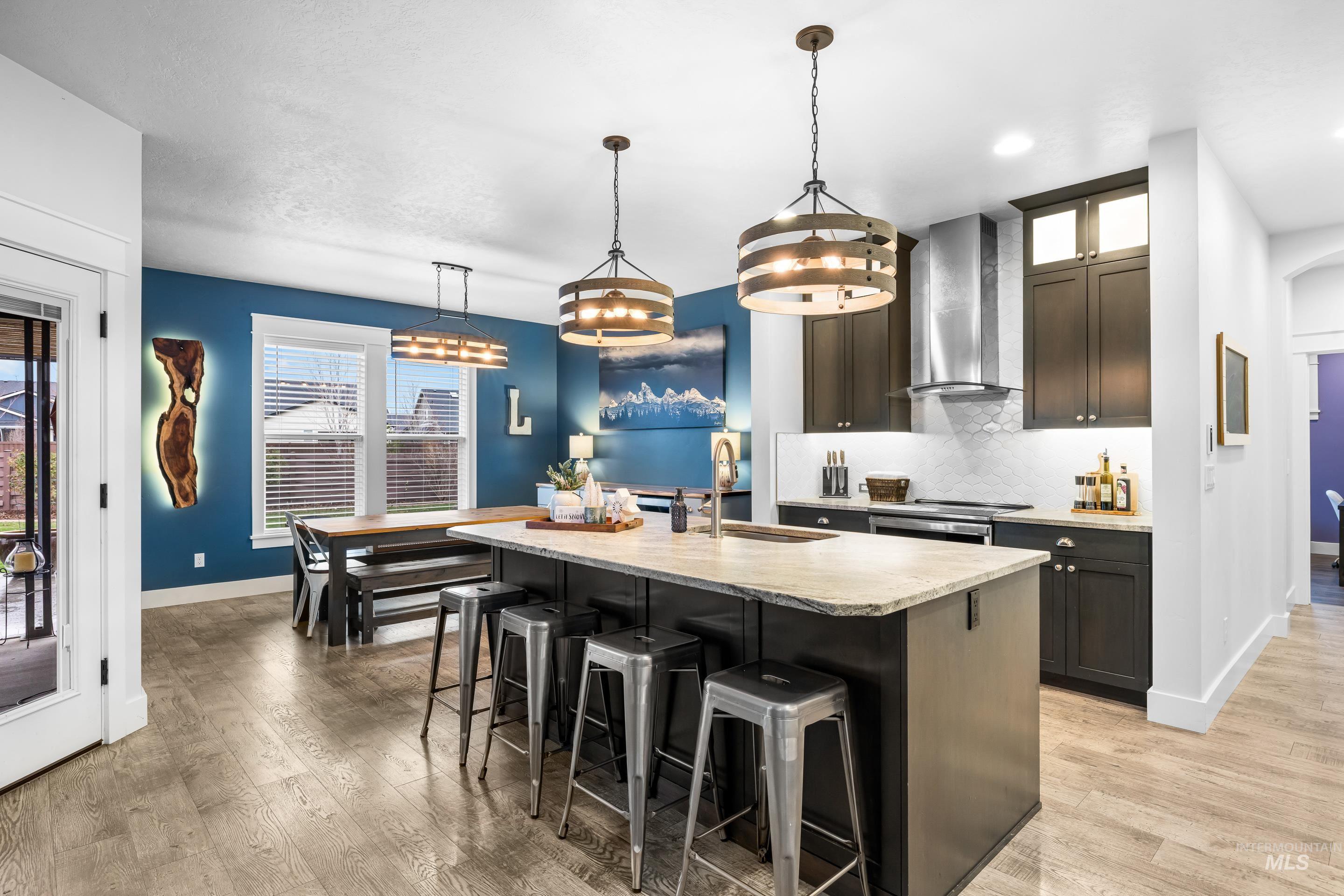 Kitchen featuring a kitchen breakfast bar, backsplash, hanging light fixtures, an island with sink, and light stone counters
