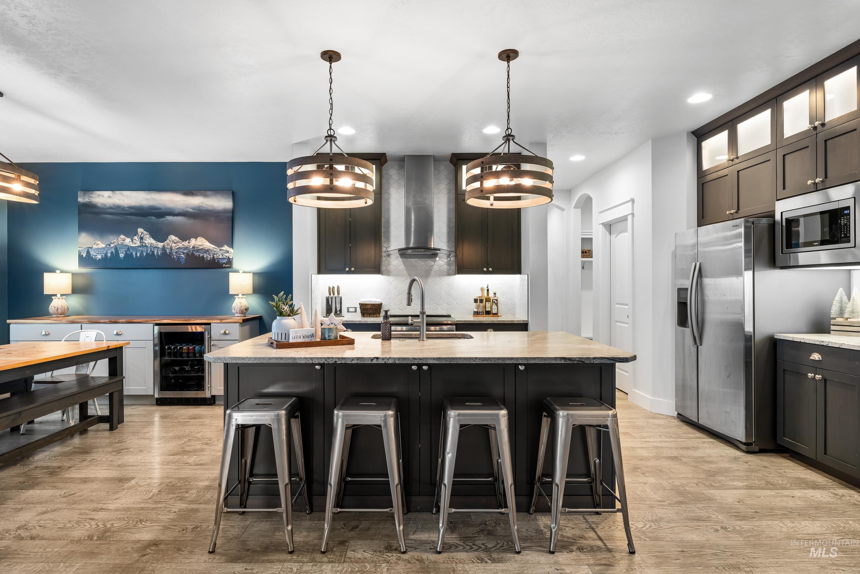 Kitchen with hanging light fixtures, a kitchen bar, beverage cooler, light stone counters, and a center island with sink