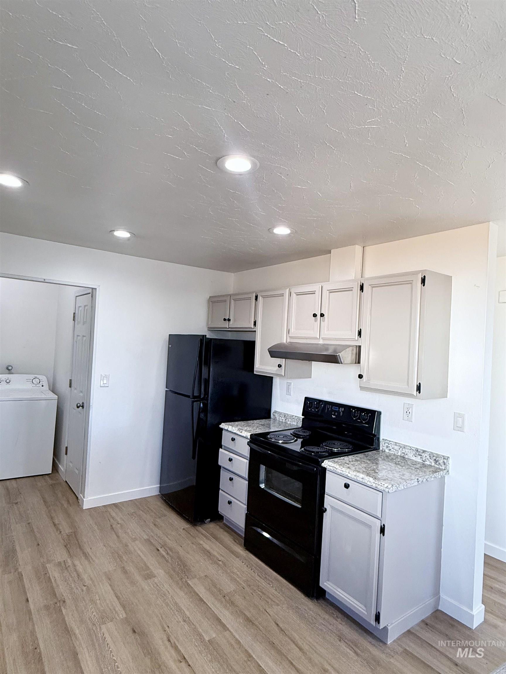 Kitchen featuring black appliances, washer / clothes dryer, light wood-style floors, recessed lighting, and under cabinet range hood