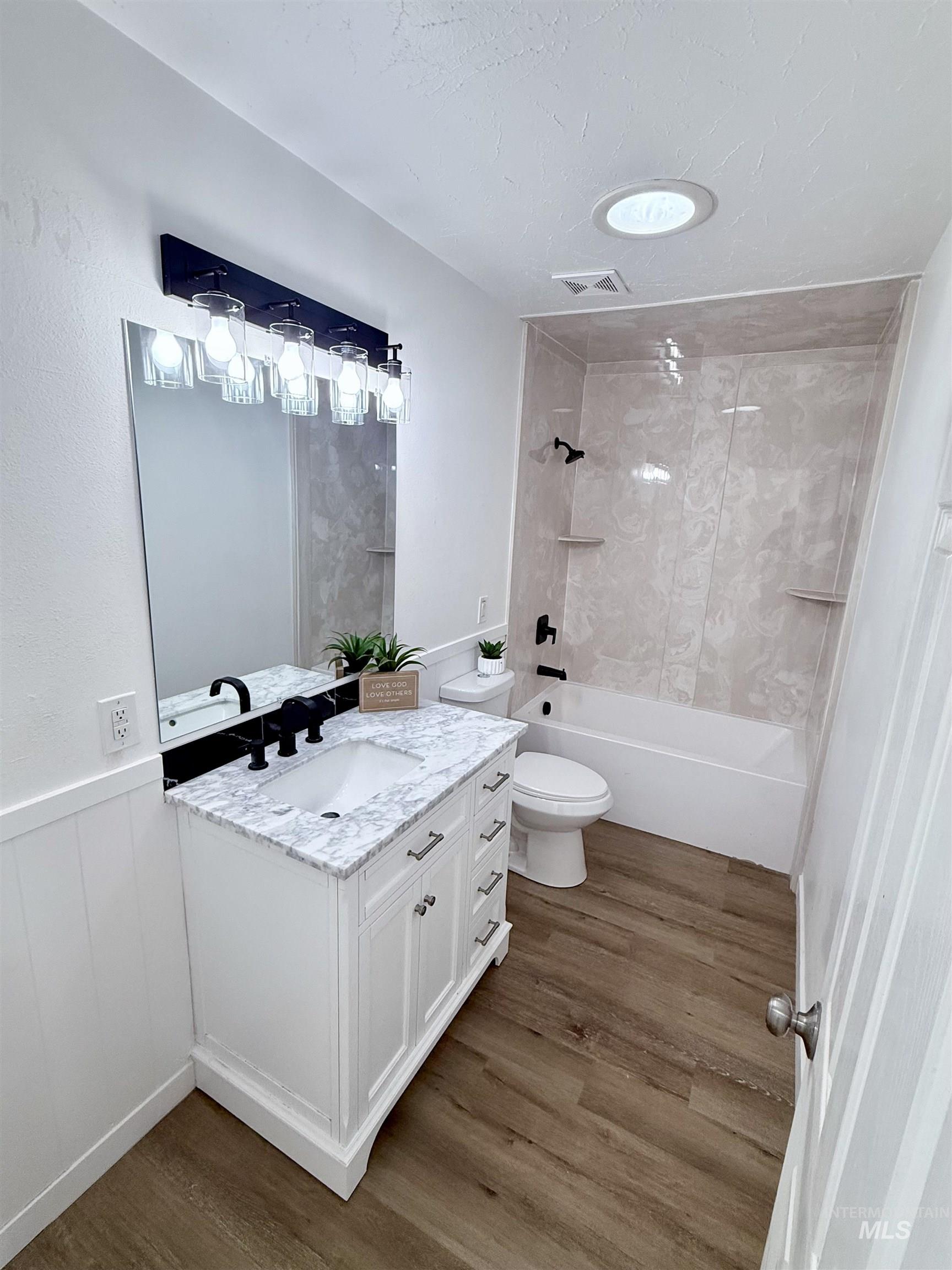 Bathroom featuring shower / tub combination, vanity, dark wood-style flooring, wainscoting, and a textured ceiling