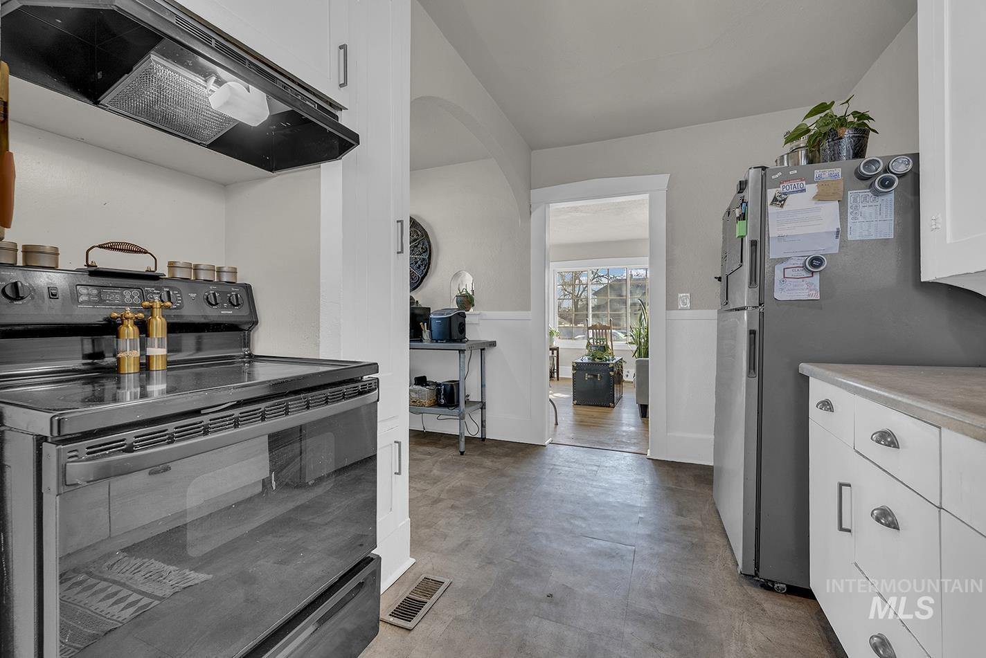 Kitchen with black range with electric cooktop, extractor fan, white cabinetry, and freestanding refrigerator