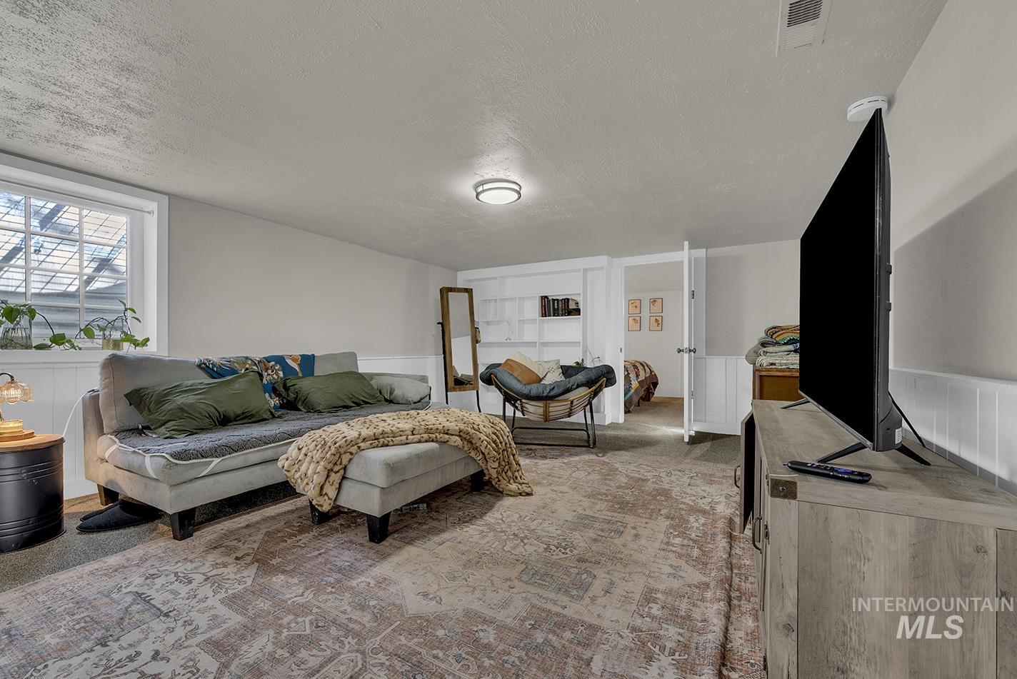 Carpeted living area featuring a textured ceiling and wainscoting